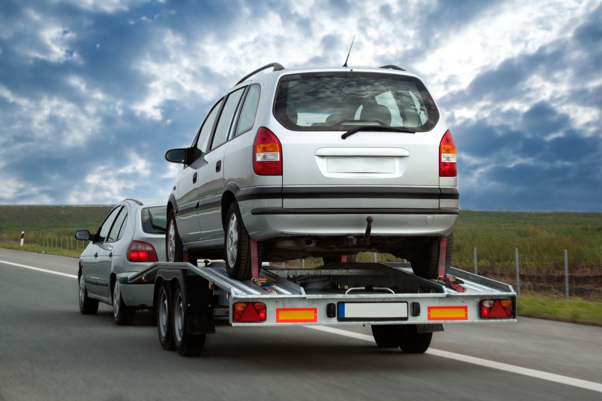Silver SUV on a car carrier trailer driving on a highway under cloudy skies