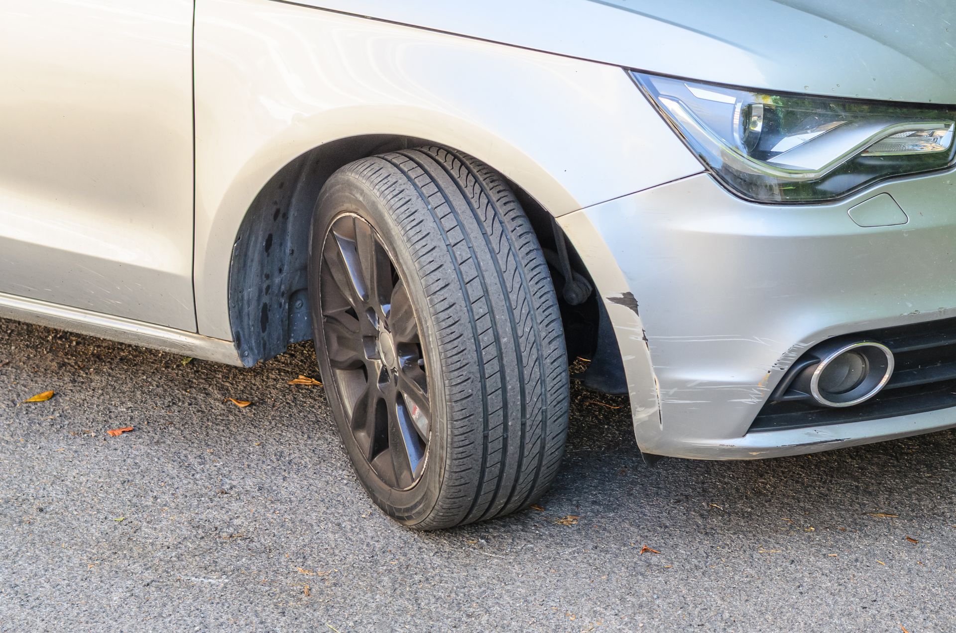 Close-up of a silver car with a front tire turned outward, parked on pavement.
