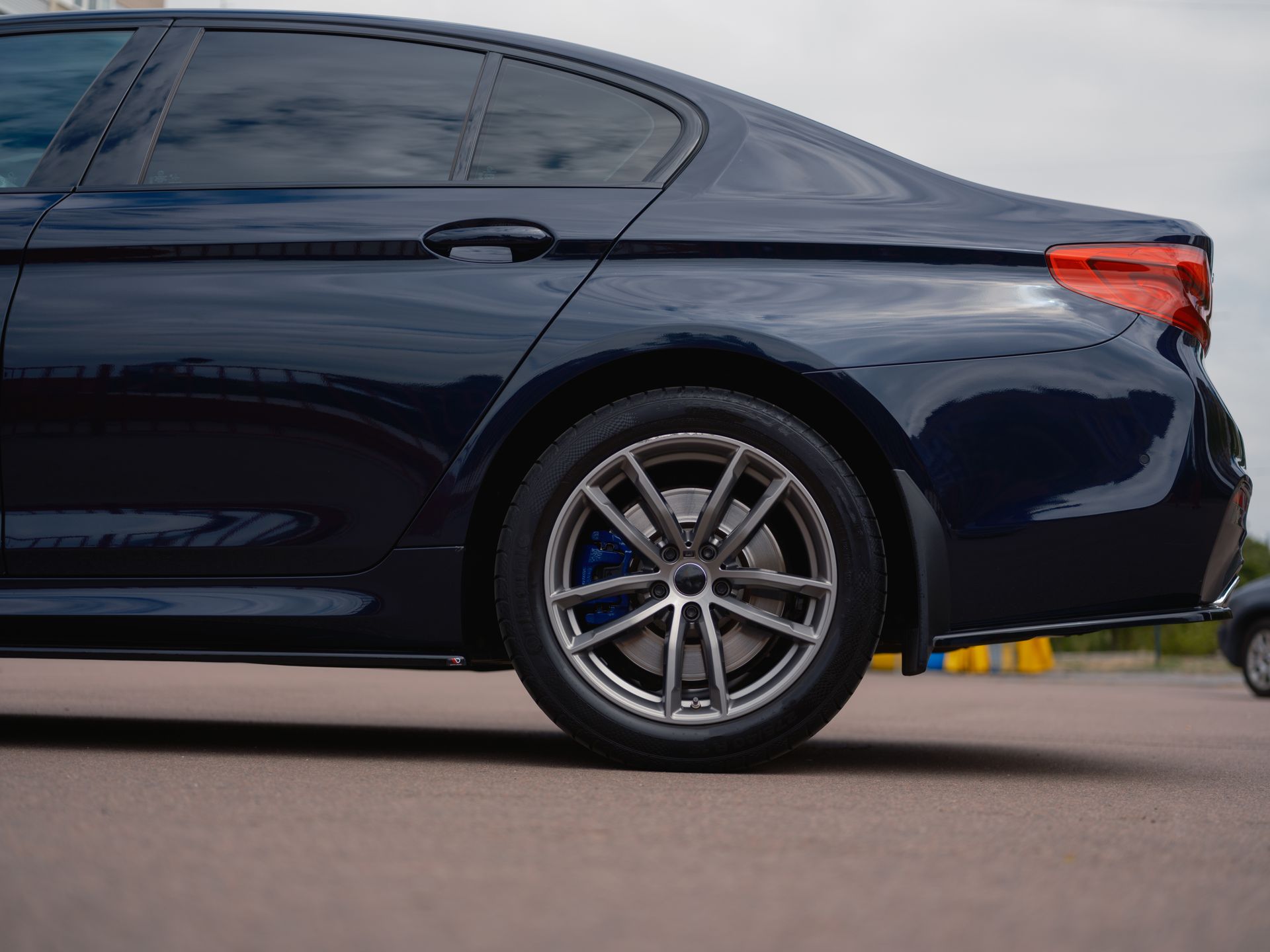 Dark blue sedan in side view, parked on pavement with rear wheel and taillight visible.
