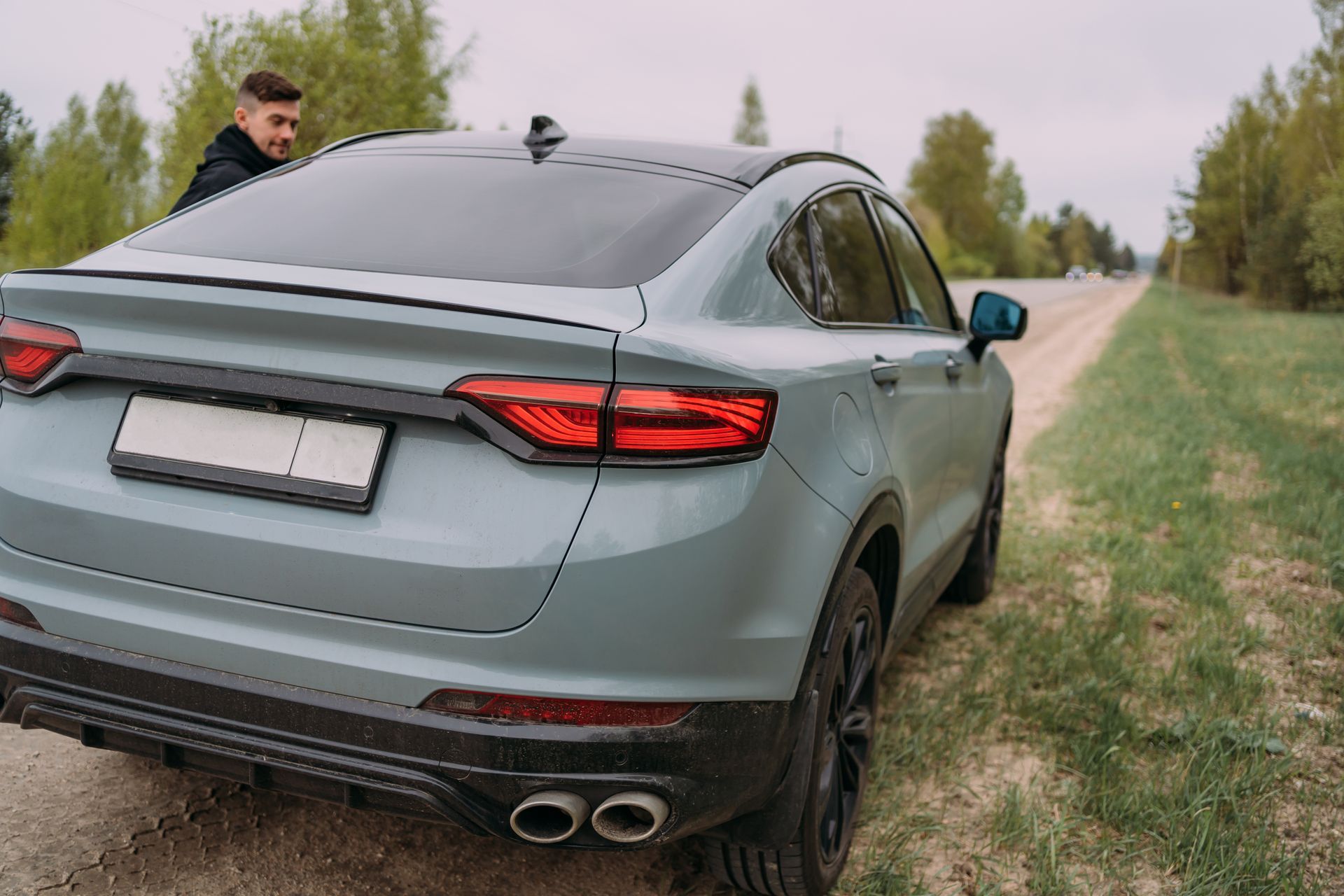 Gray sedan parked on a grassy roadside with a man standing by the rear left side