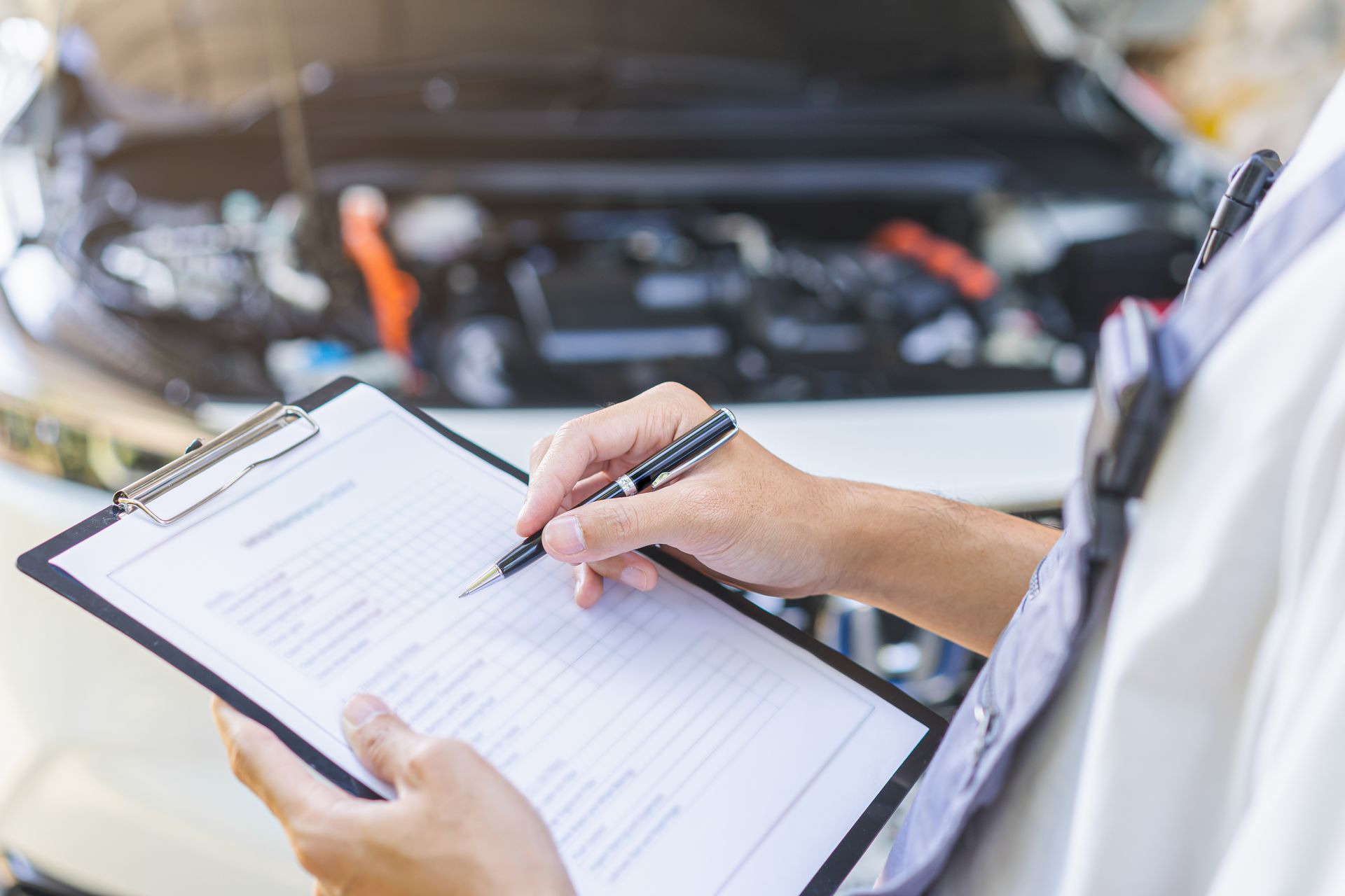 Mechanic inspecting a clipboard in front of an open car hood