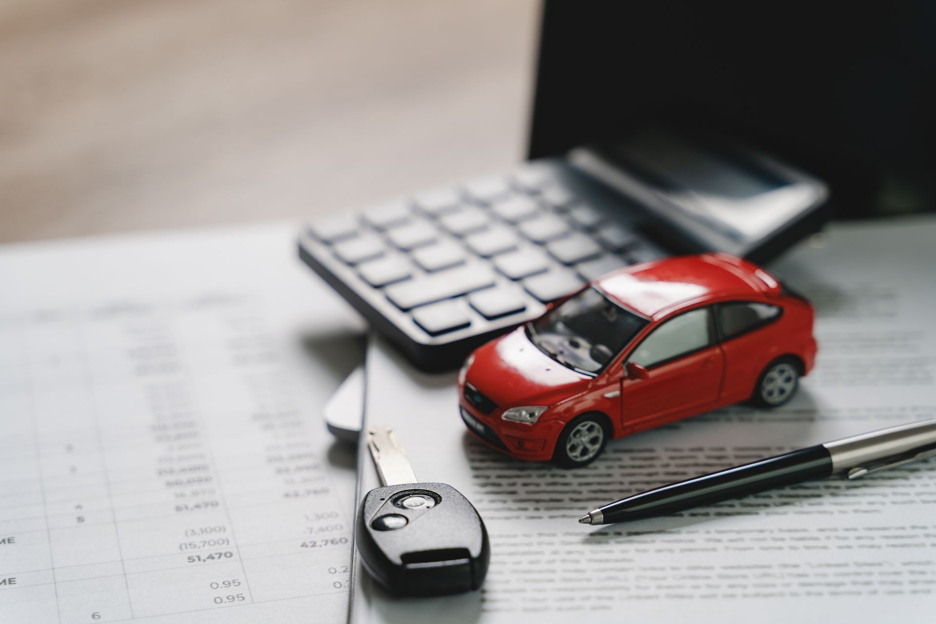 Red toy car, calculator, keys, and pen on paperwork, suggesting car insurance or expenses.