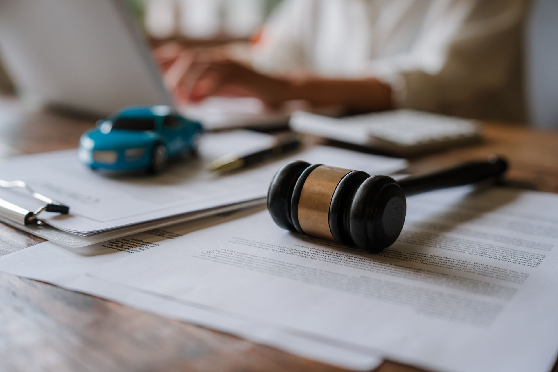 Lawyer’s desk with gavel, car model, and papers in soft focus behind a notebook