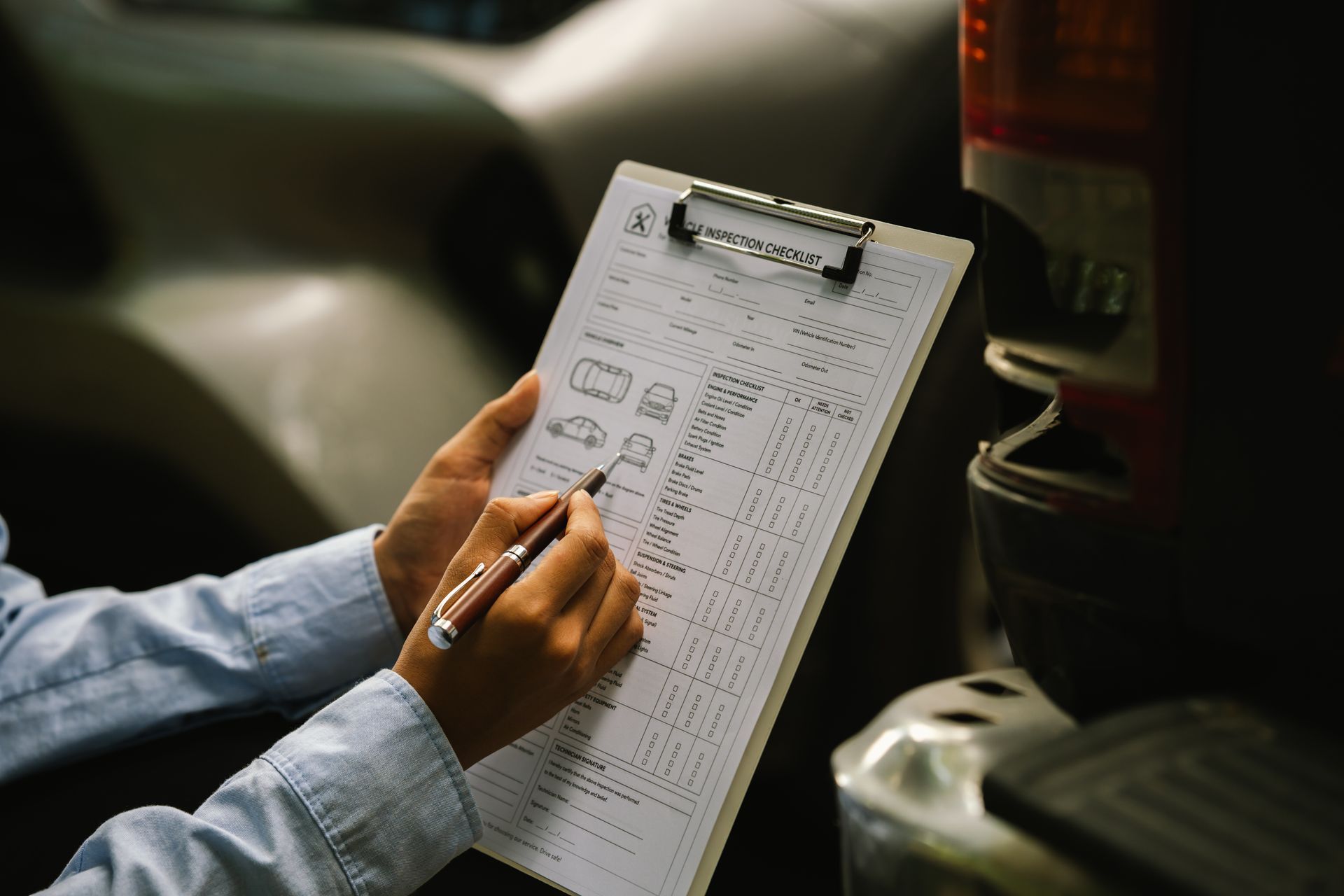 Hand holding a clipboard and pen, filling out a form in a dimly lit car interior.