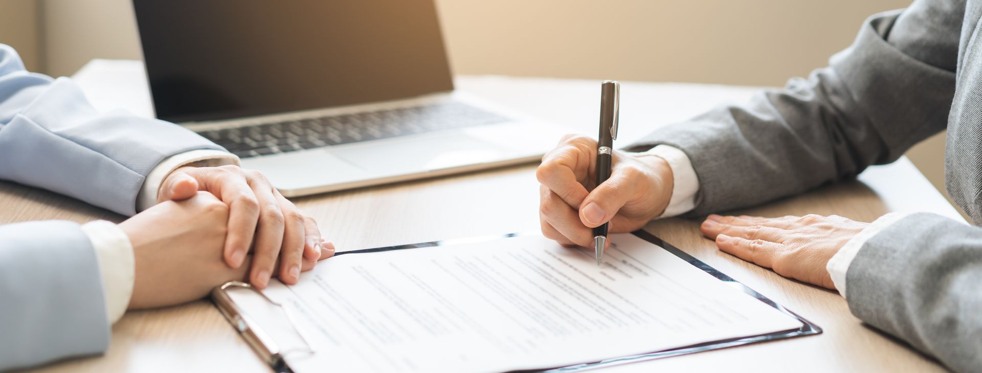Hands signing a document on a desk with a laptop in the background