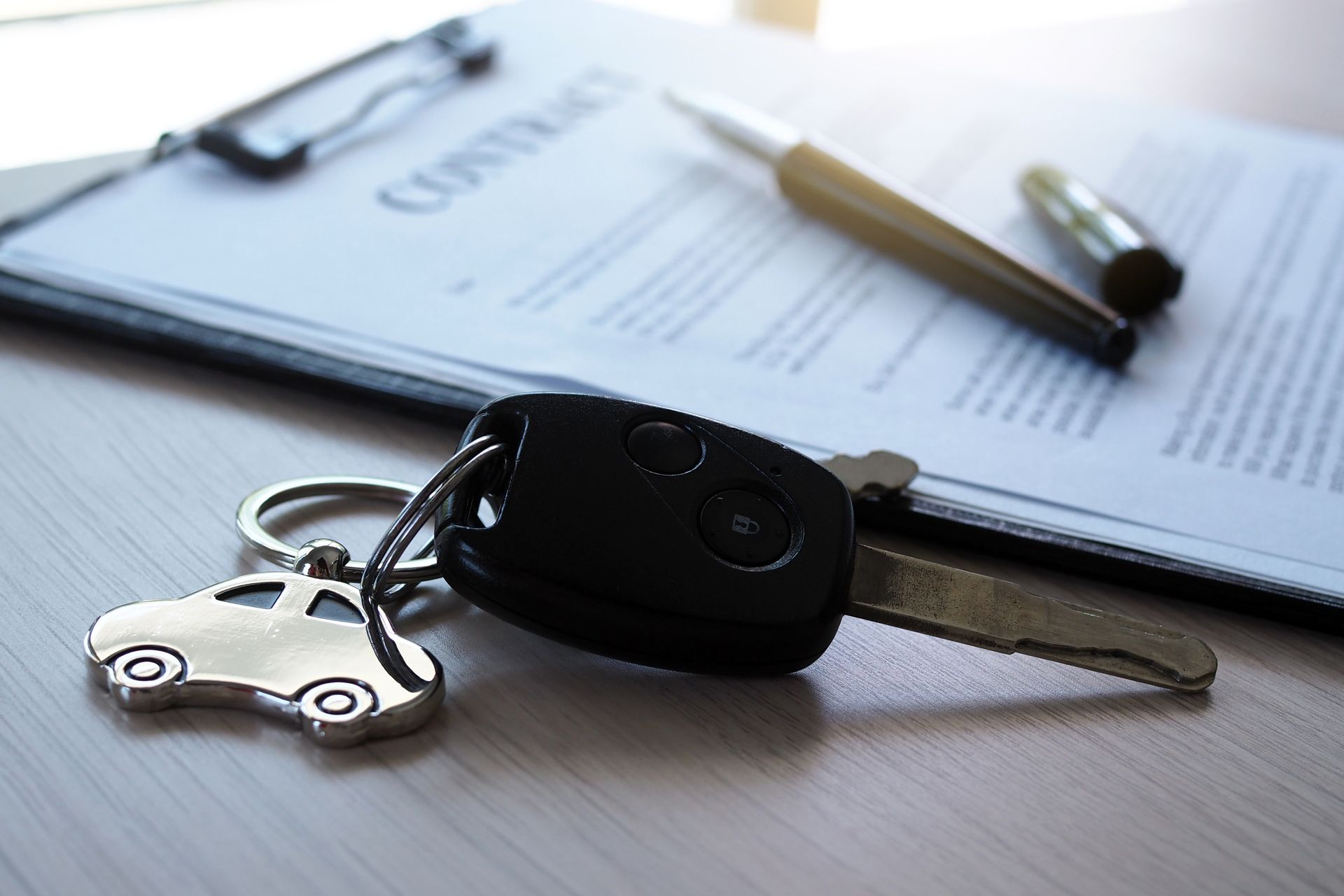 Car key and remote on a desk with paperwork and a pen in the background Car key and remote on a desk with paperwork and a pen in the background