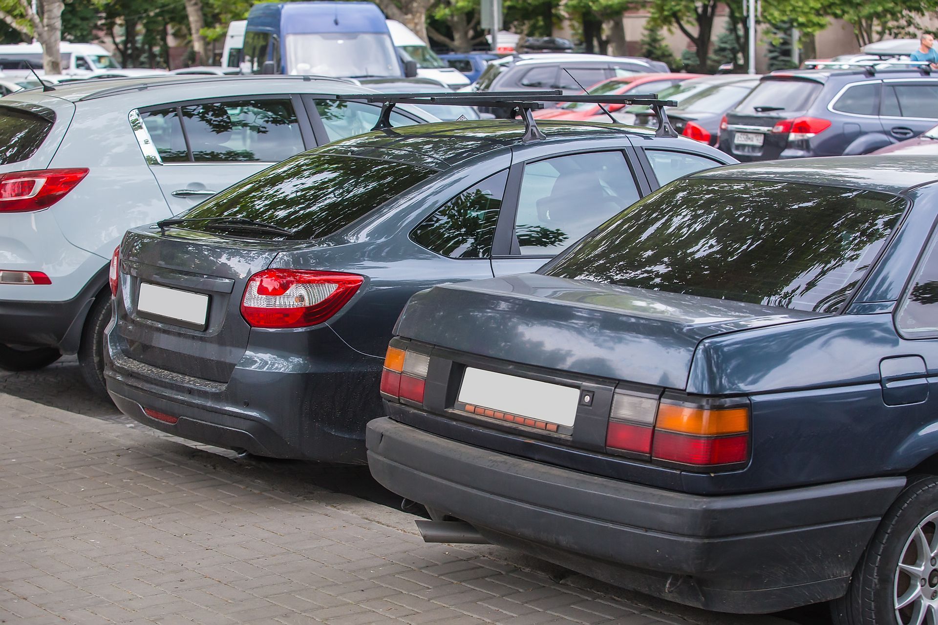 Parked cars in a crowded lot, including a dark sedan in the foreground and white SUVs behind it Parked cars in a crowded lot, including a dark sedan in the foreground and white SUVs behind it