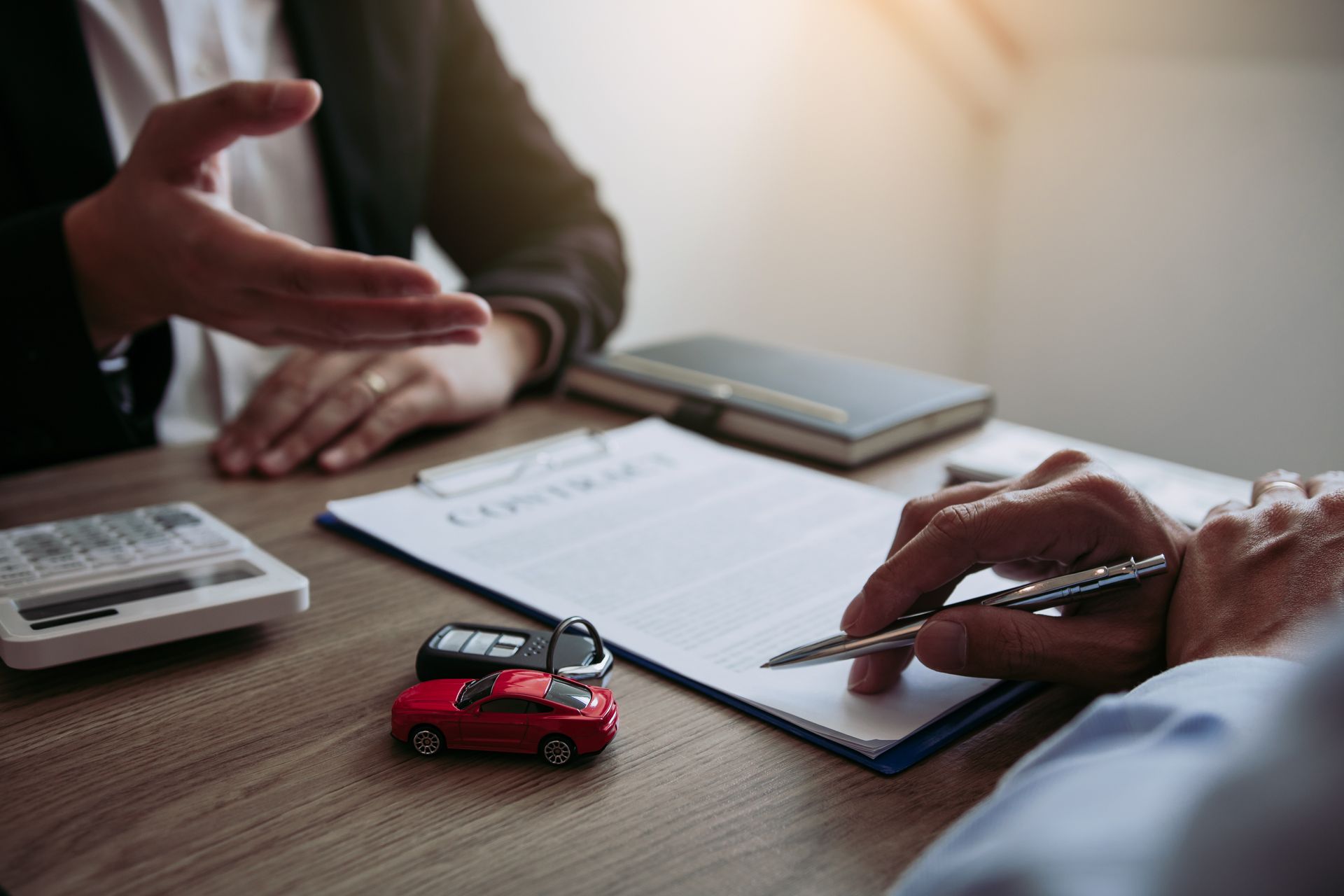 Business meeting with hands over documents, calculator, and toy car on a desk