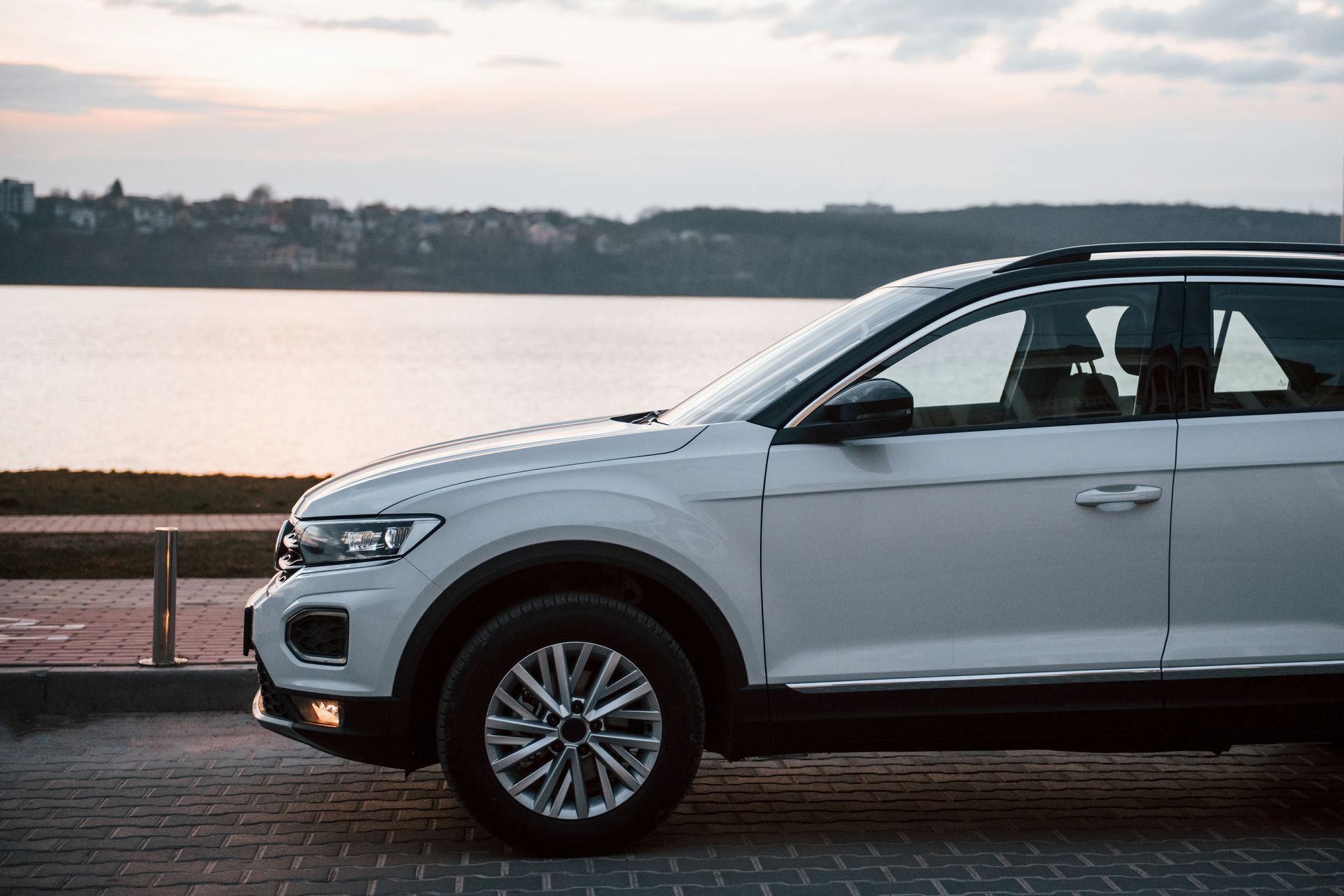 White SUV parked by a waterfront at sunset, with a person visible in the driver’s seat.