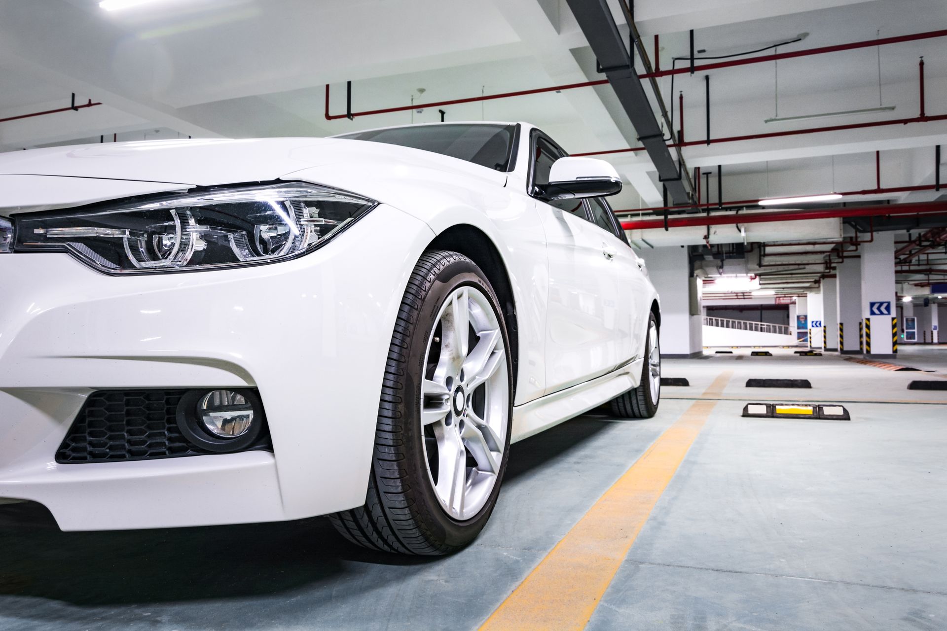 White sedan parked in a bright indoor garage, front-left view with silver wheels and yellow lane markings