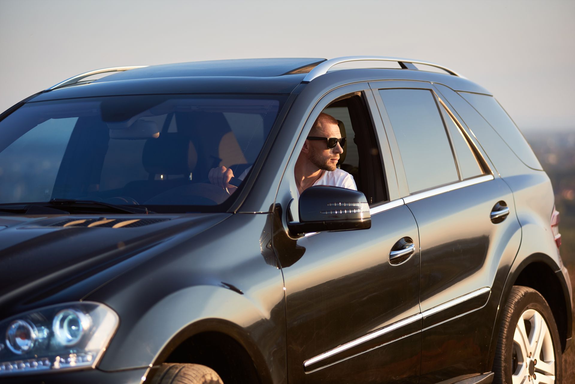Driver leaning out of a black SUV window, smiling while driving on a sunny road. Driver leaning out of a black SUV window, smiling while driving on a sunny road.