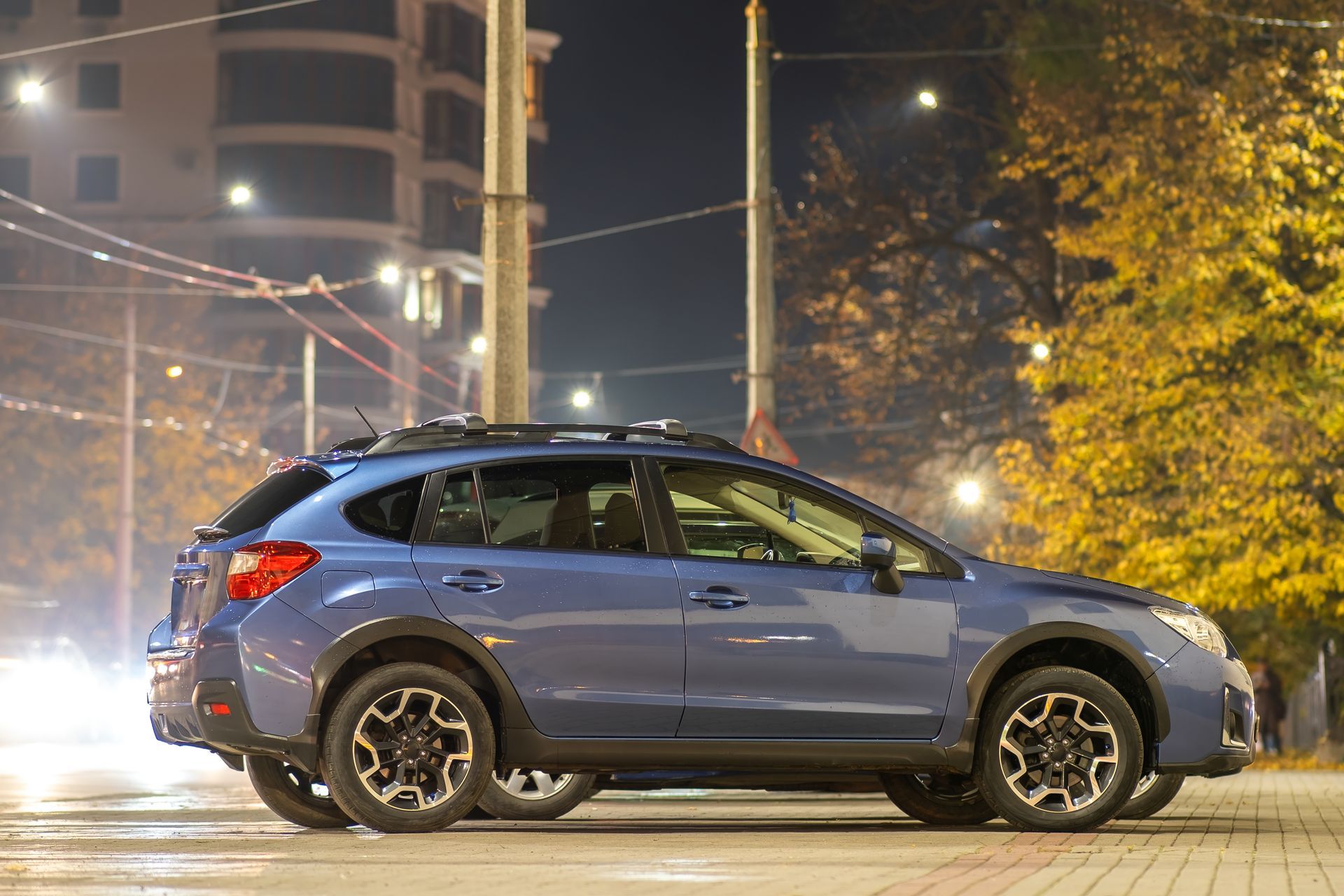 Blue SUV parked at night on a city street with lights and buildings in the background