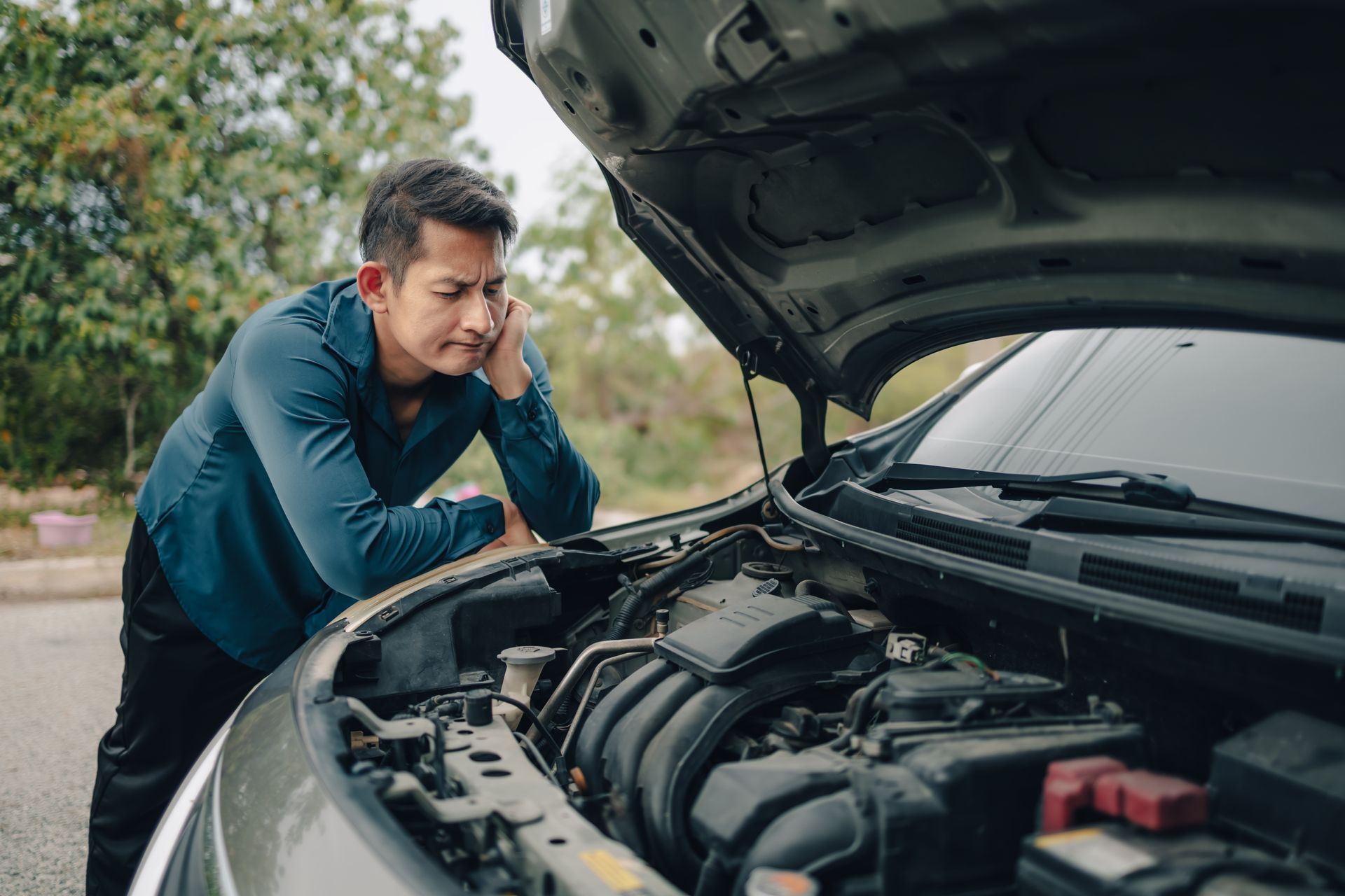 Man inspecting a car engine with the hood open on a roadside