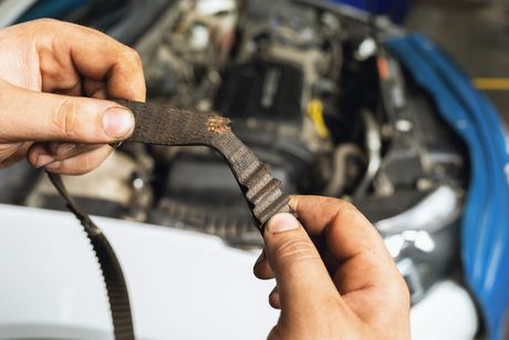 Hands holding a worn, frayed car belt in front of an open engine bay Hands holding a worn, frayed car belt in front of an open engine bay