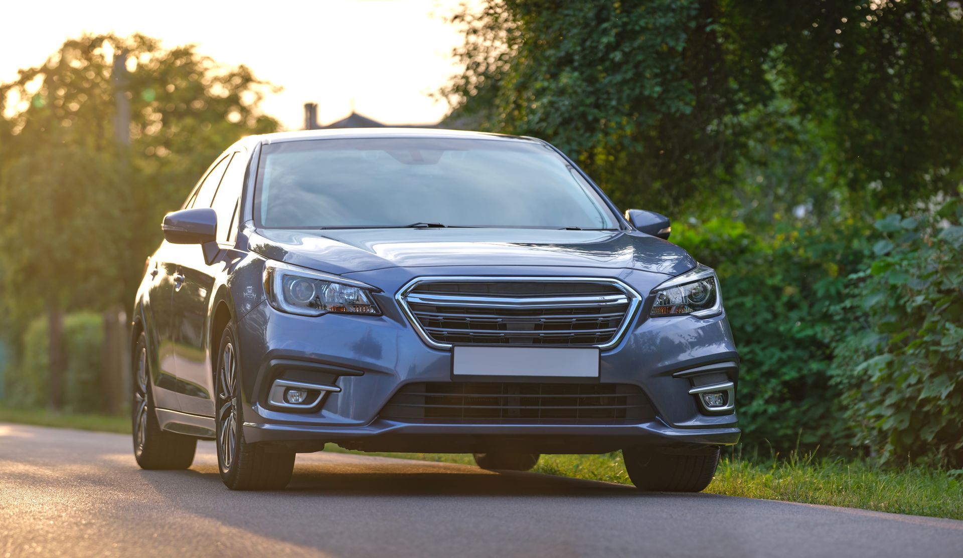 Blue sedan driving on a sunlit road beside green trees Blue sedan driving on a sunlit road beside green trees