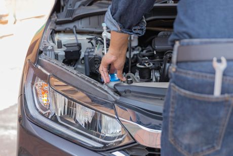 Person checking car engine under open hood, holding a blue tool near the headlight Person checking car engine under open hood, holding a blue tool near the headlight