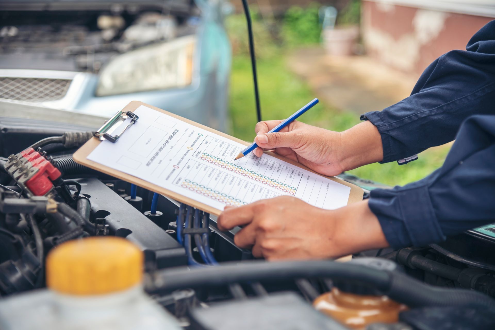 Mechanic writing on a clipboard beside an open car engine outdoors Mechanic writing on a clipboard beside an open car engine outdoors