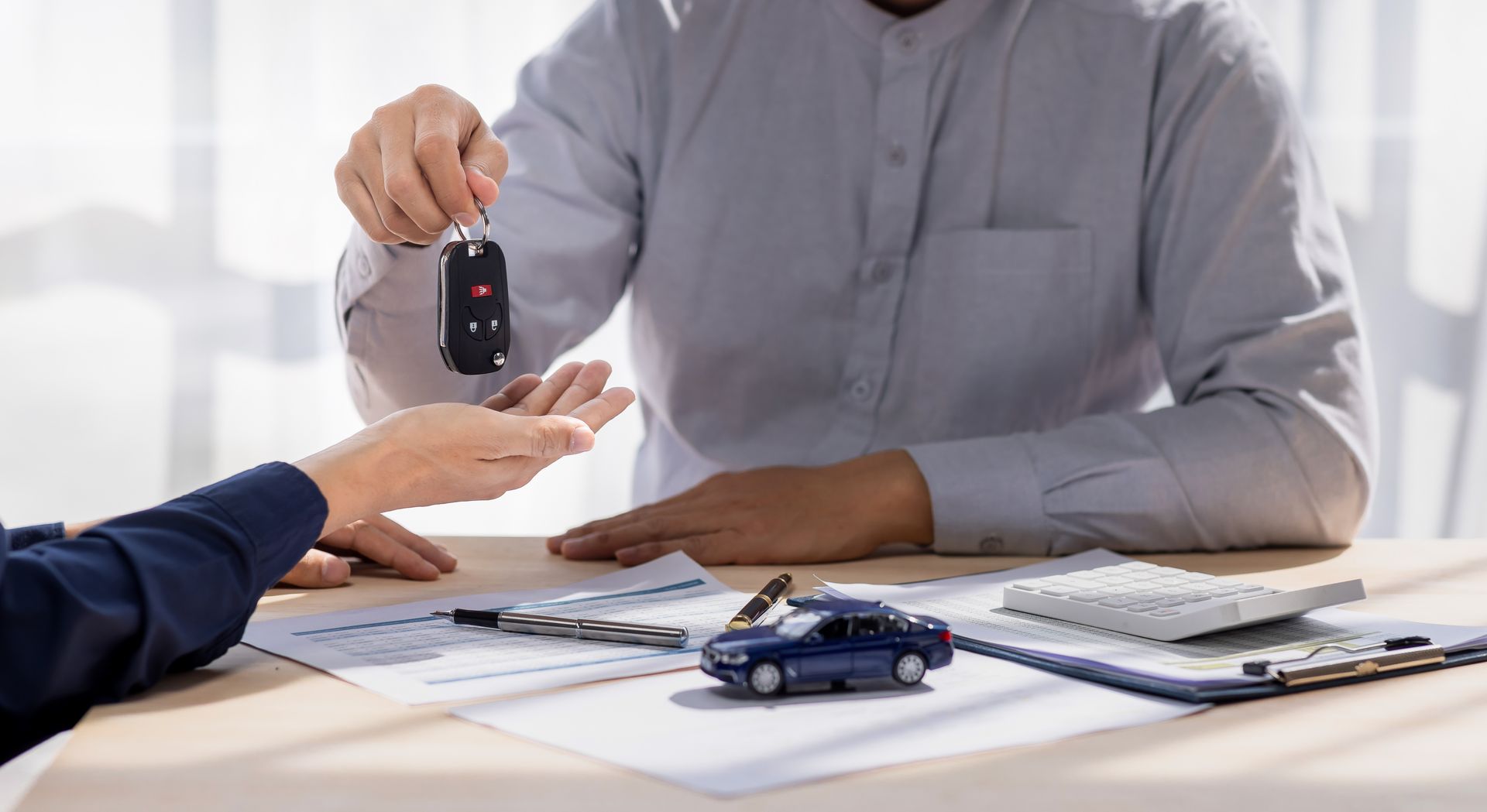 Car key handed over at a desk with contract papers, calculator, and toy car, suggesting a car sale or rental Car key handed over at a desk with contract papers, calculator, and toy car, suggesting a car sale or rental