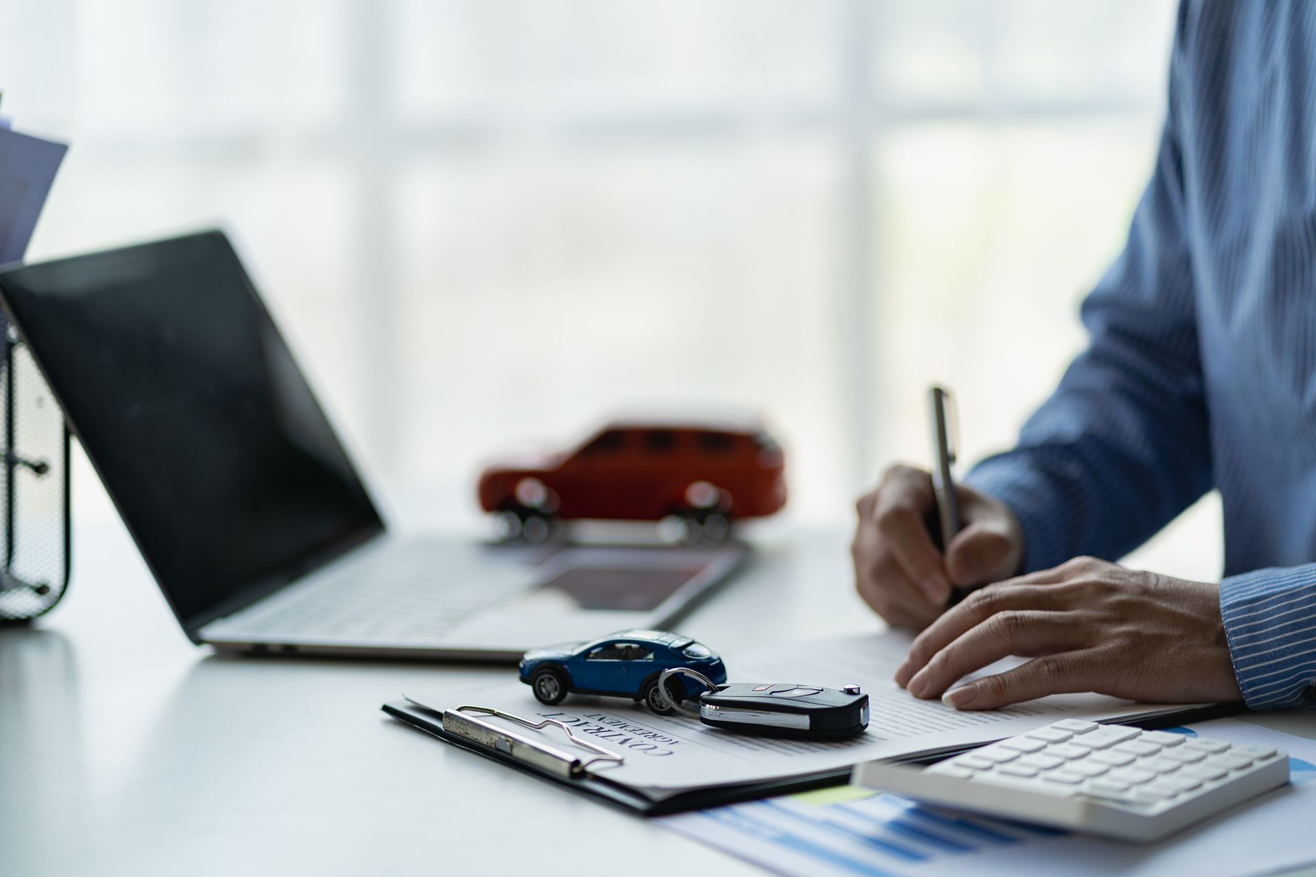 Person reviewing documents beside laptop and toy car on a desk