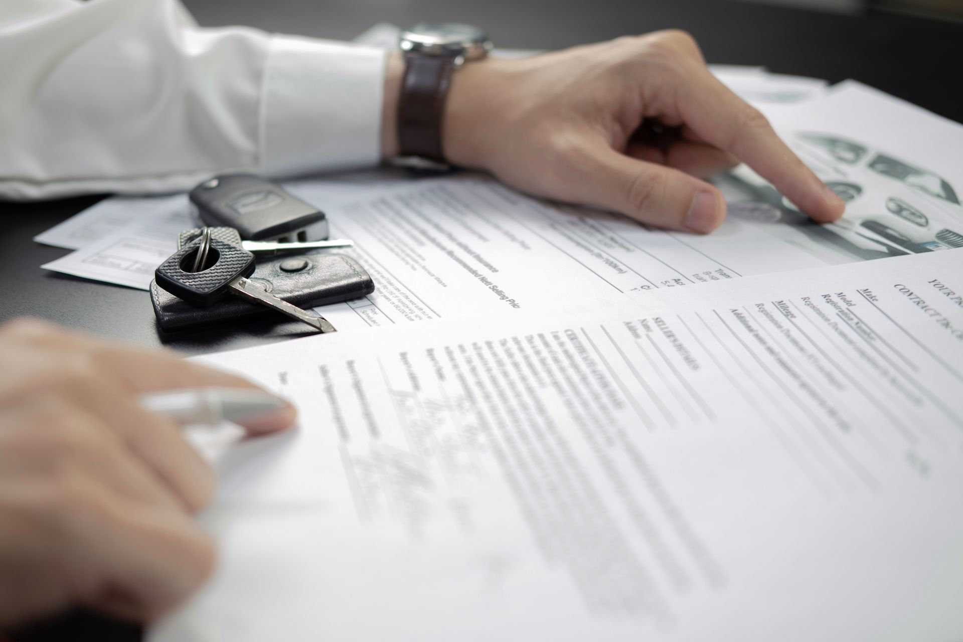 Hands reviewing paperwork with car keys on a desk in a bright office setting
