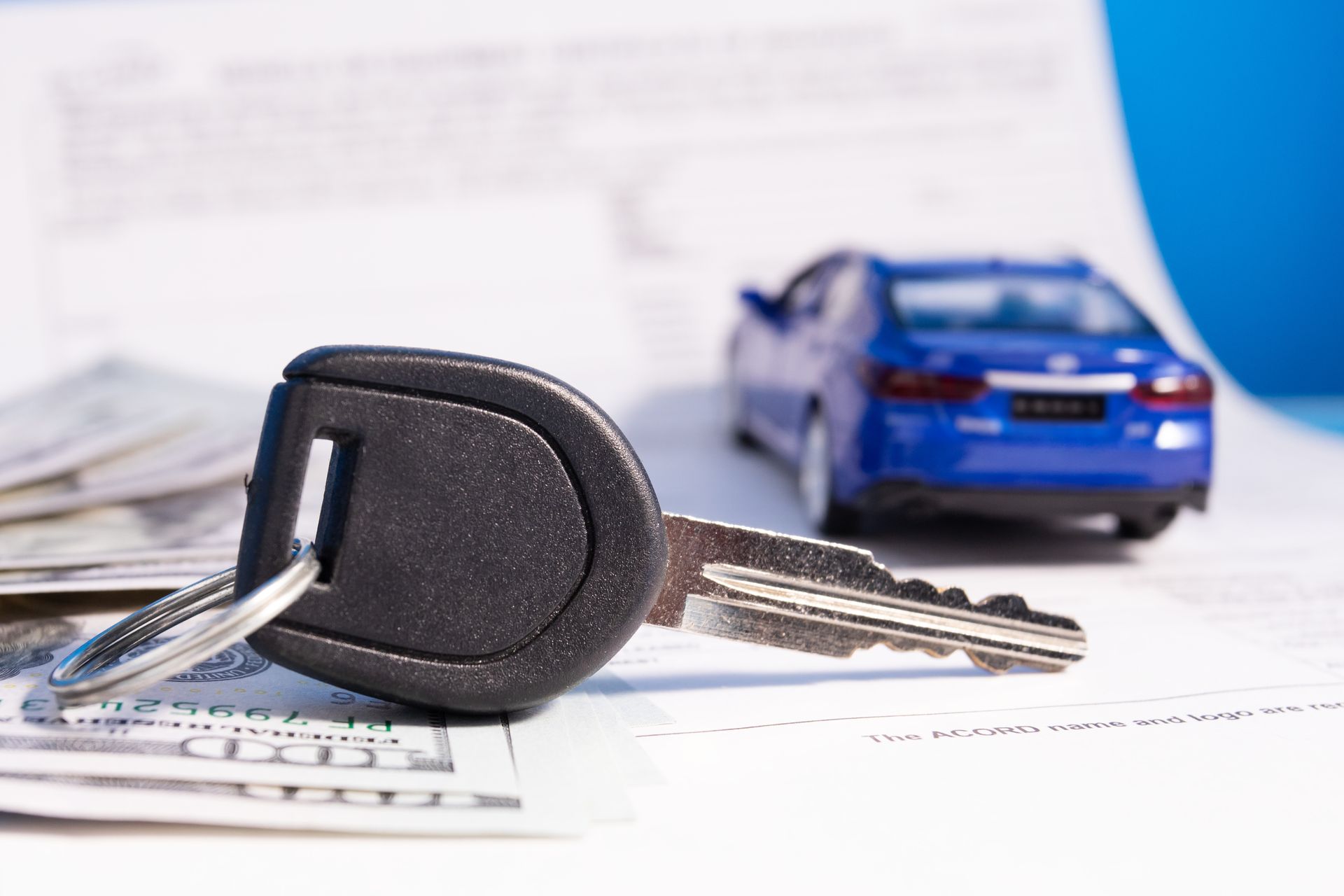 Car key with fob and silver keys beside a blue toy car on paperwork