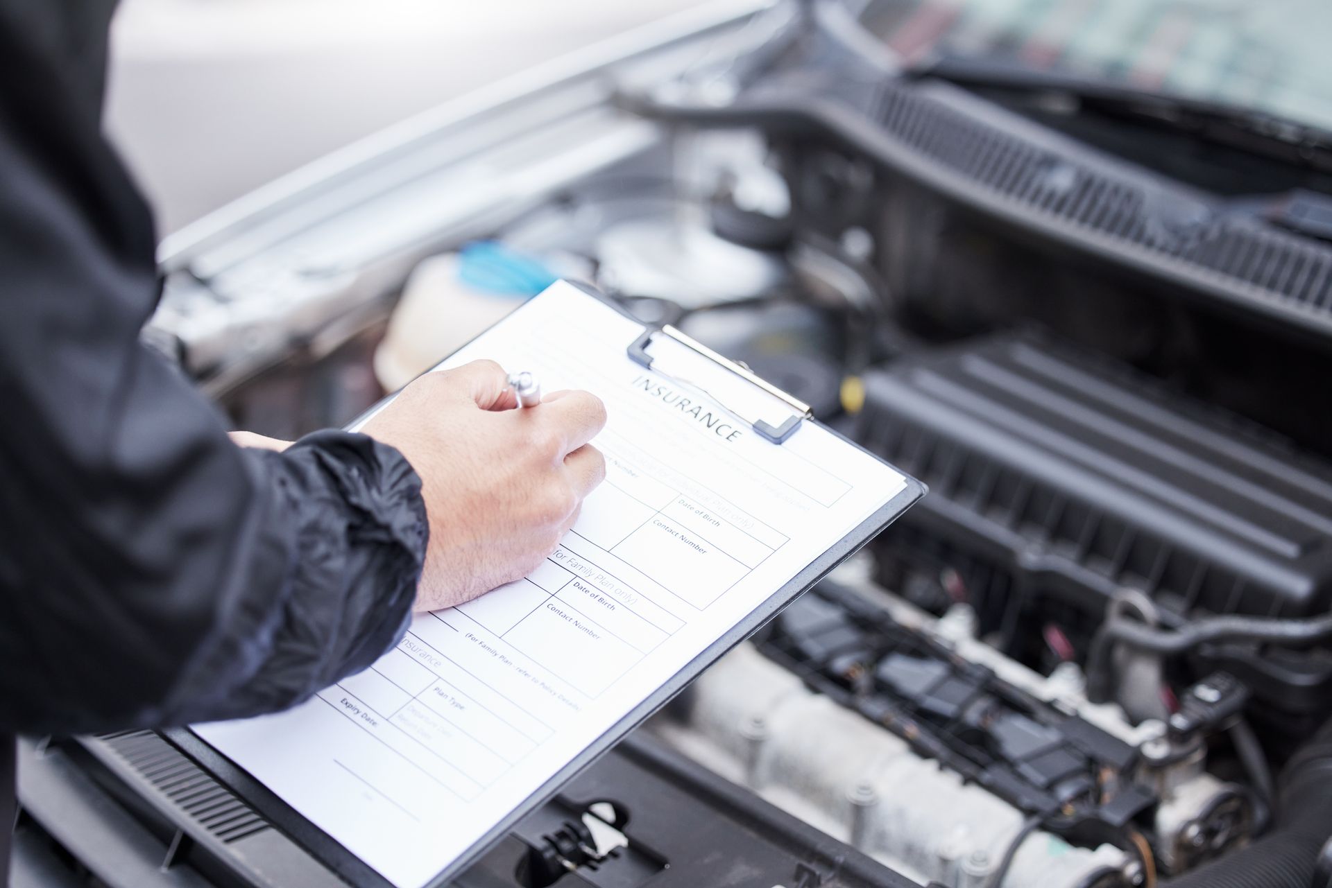 Person checking a car engine with a clipboard and pen