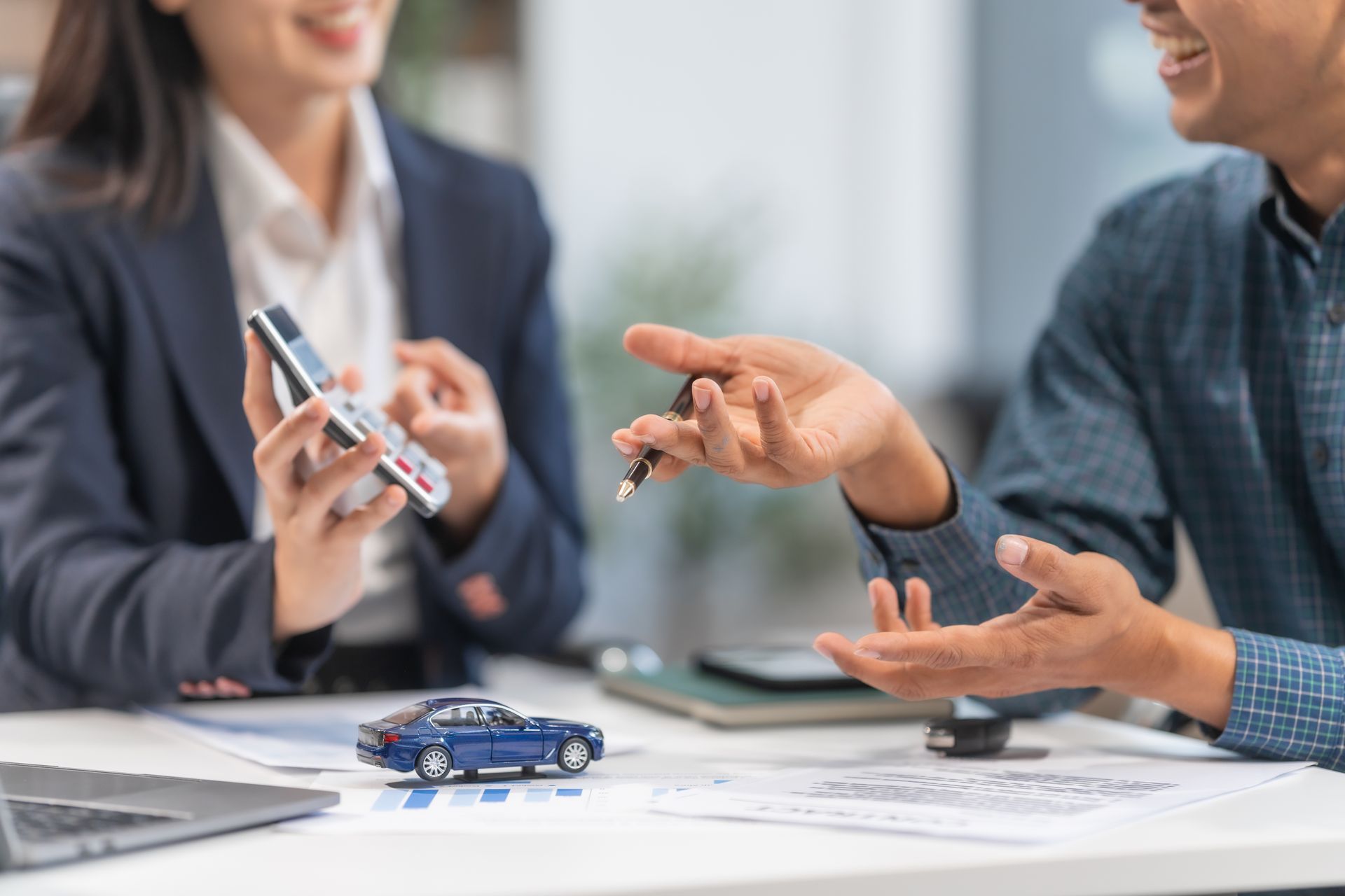 Two people discussing a blue toy car on a table in an office setting