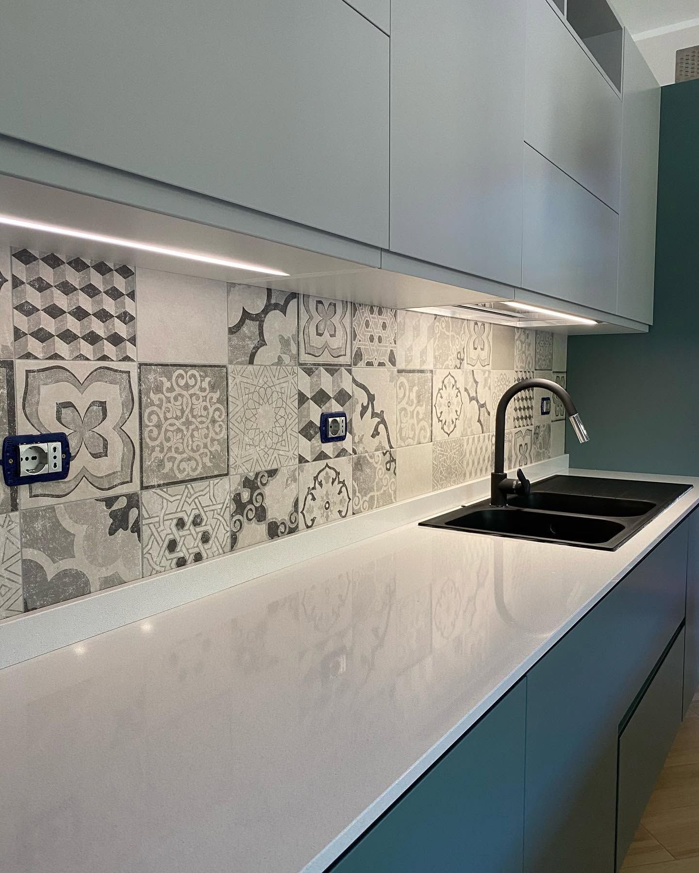 Piano di lavoro moderno in cucina con paraschizzi in piastrelle decorative, mobili bianchi, lavello nero e rubinetto cromato