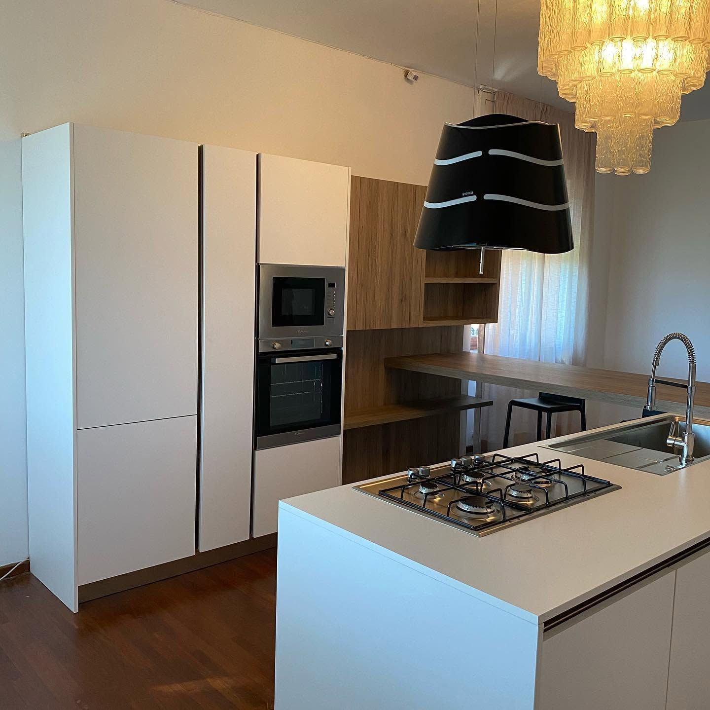 Cucina moderna con isola bianca, forno a incasso, mobili in legno e lampada a sospensione nera