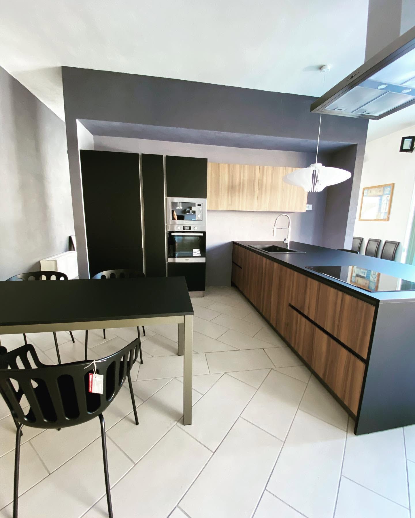 Cucina moderna con mobili in legno, isola nera, pavimento piastrellato e lampada a sospensione