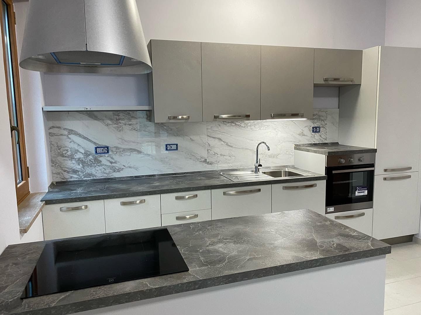 Cucina moderna con mobili grigi, paraschizzi in marmo, fornelli e lavello in acciaio inox e piani di lavoro scuri