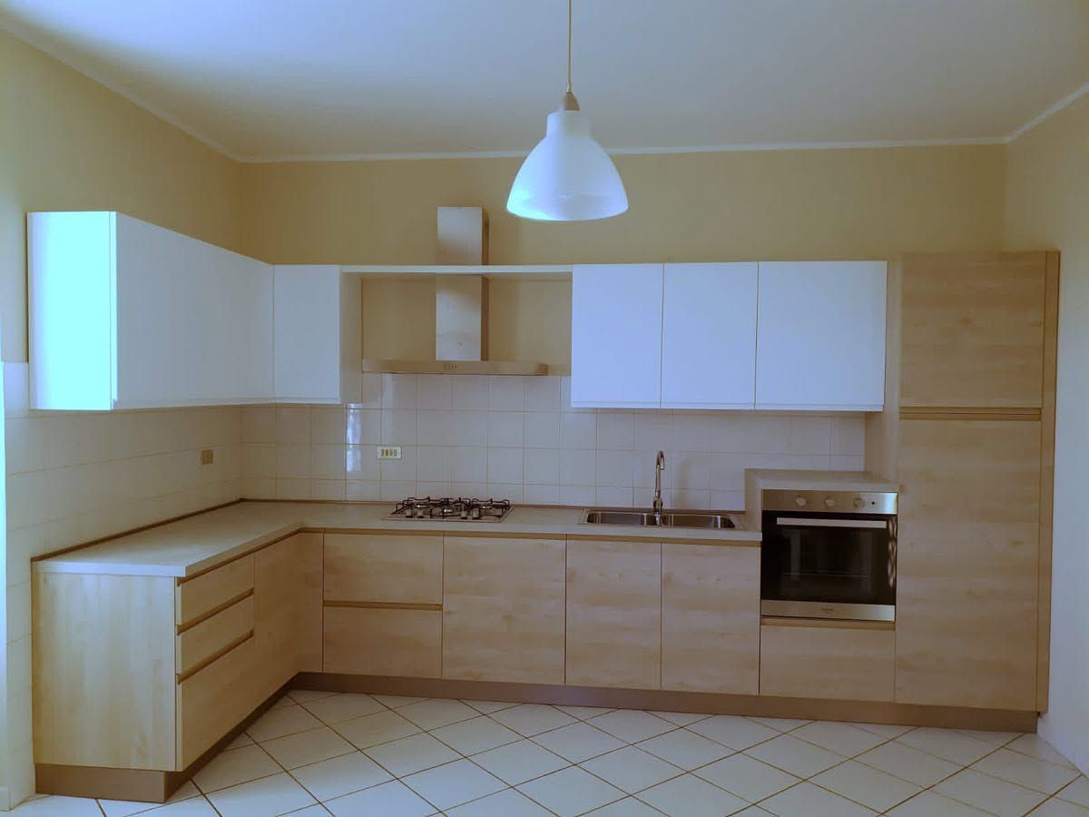 Cucina moderna beige con mobili bianchi, piani di lavoro in legno, forno a incasso e pavimento piastrellato