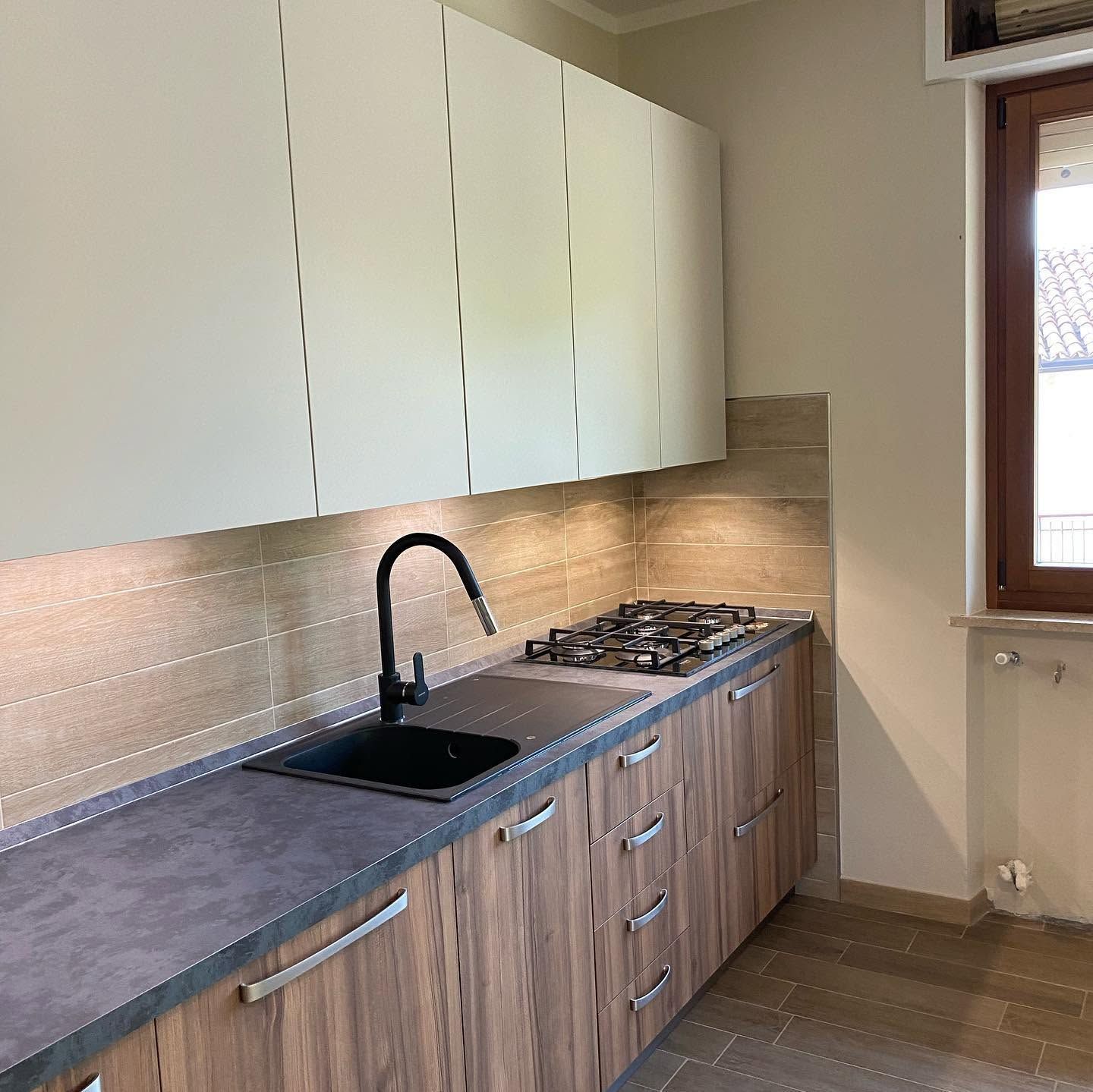 Cucina moderna con mobili in legno, lavello e rubinetto neri, piano cottura a gas e pensili bianchi