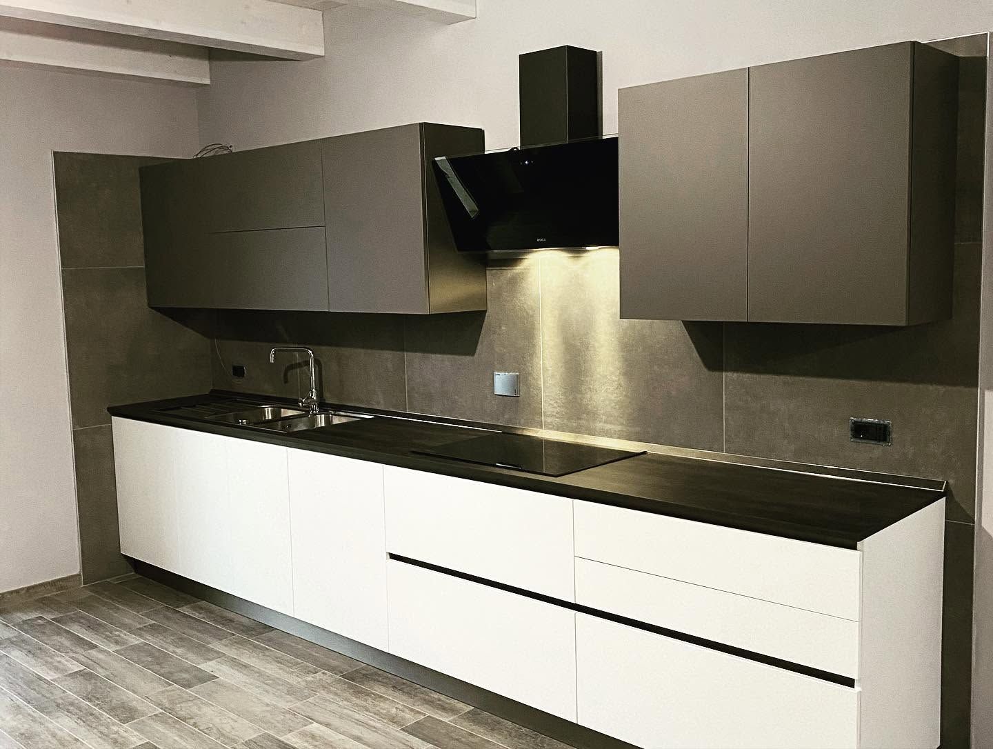 Cucina moderna con mobili bassi bianchi, piani di lavoro scuri e mobili pensili grigi sotto una cappa in acciaio inox