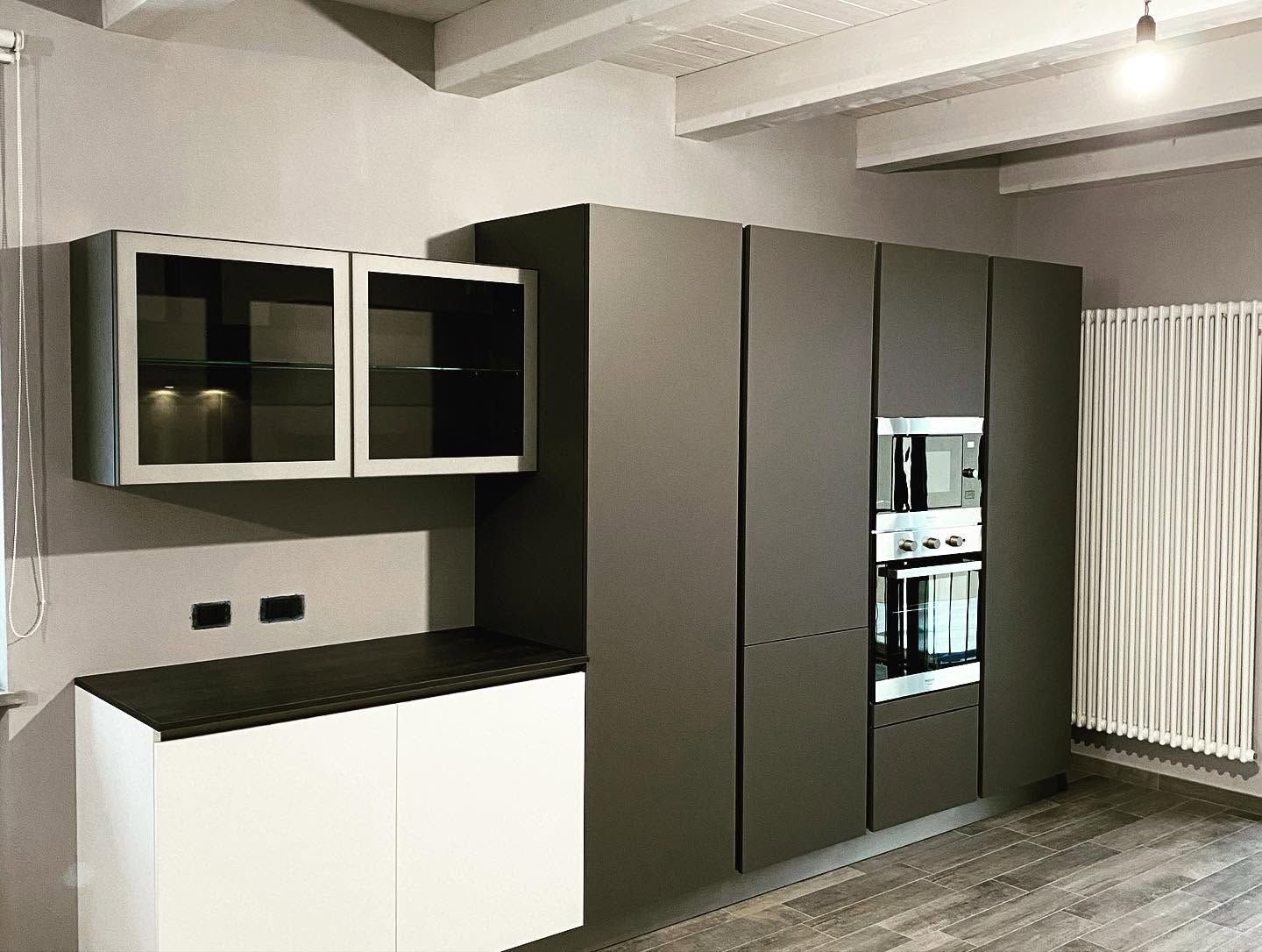 Cucina moderna con mobili grigi, basi bianche e frigorifero a incasso accanto a una finestra