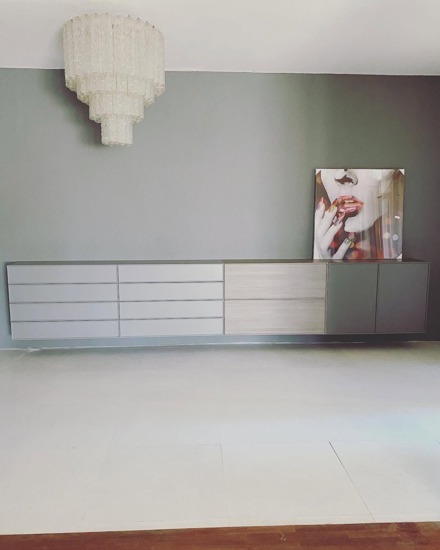Stanza moderna con una parete grigia, un lampadario bianco, un mobile contenitore basso bianco e un’opera d’arte incorniciata sulla destra.