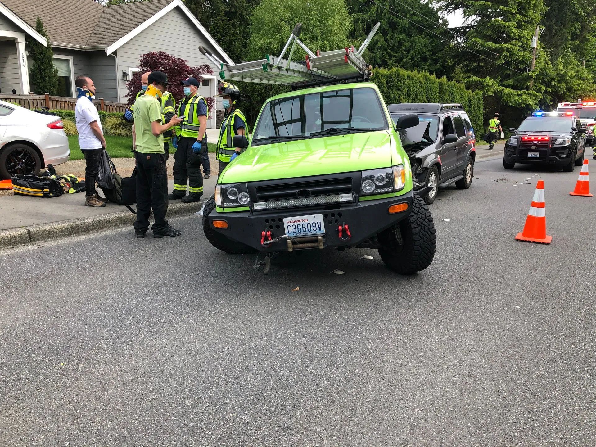 Lime green SUV with front damage, emergency responders on street.