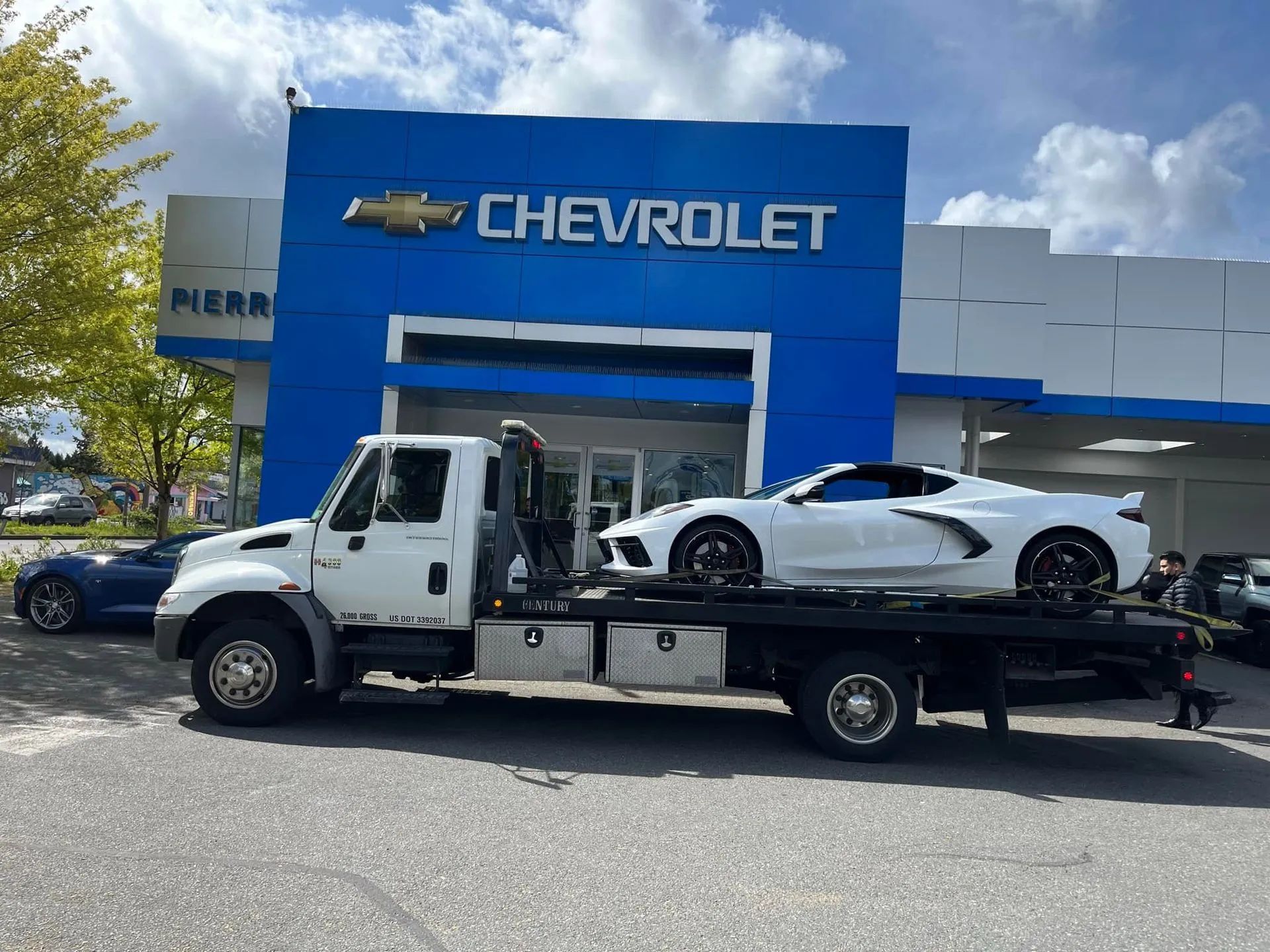 Tow truck hauling a white sports car in front of a Chevrolet dealership