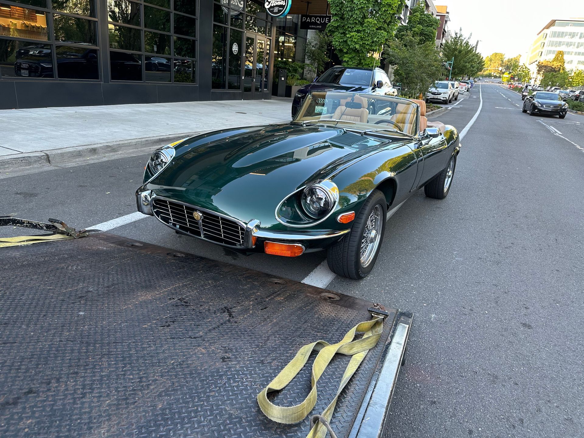 A green sports car is being towed down a city street.