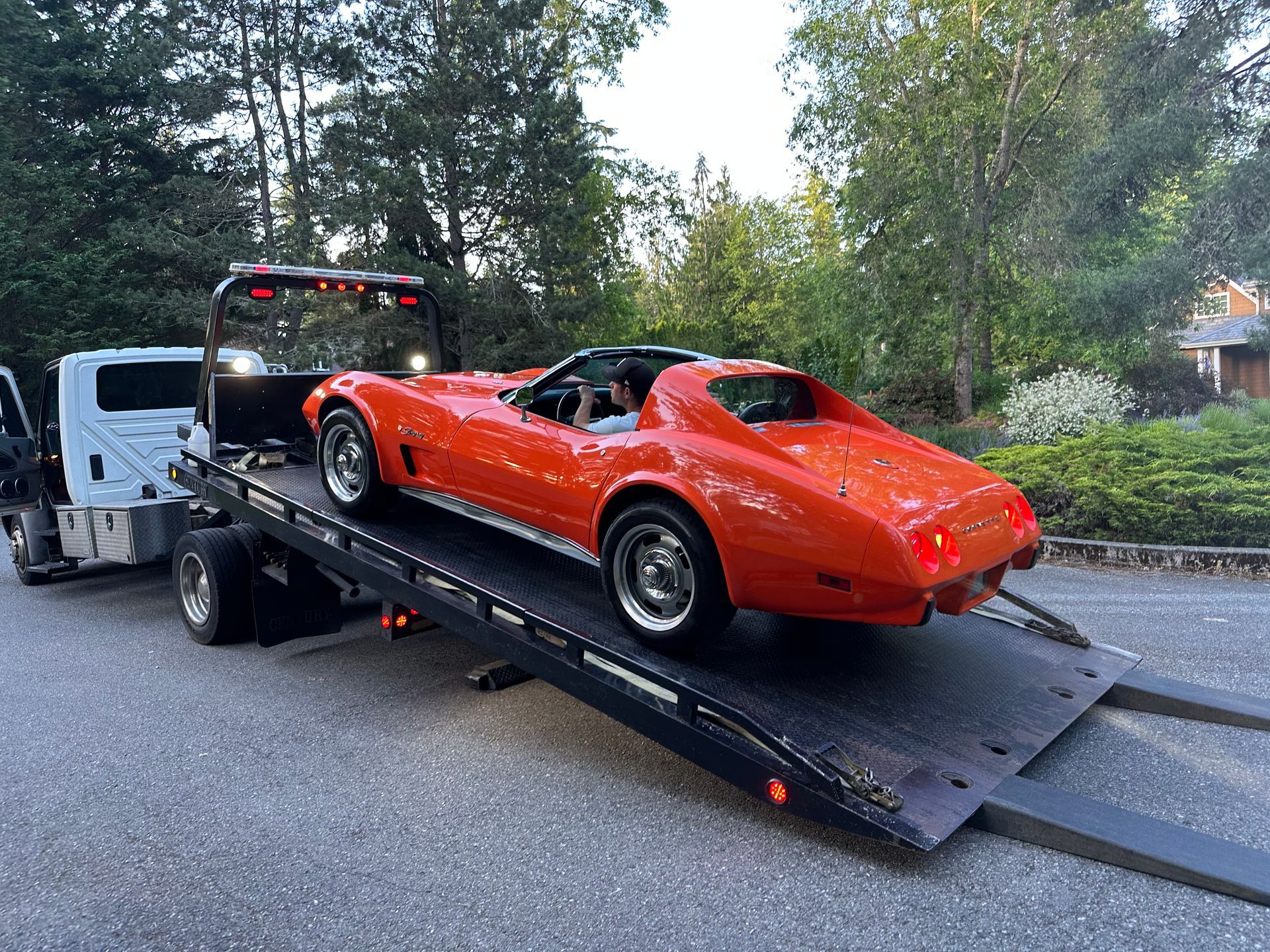 A red corvette is being towed by a tow truck.