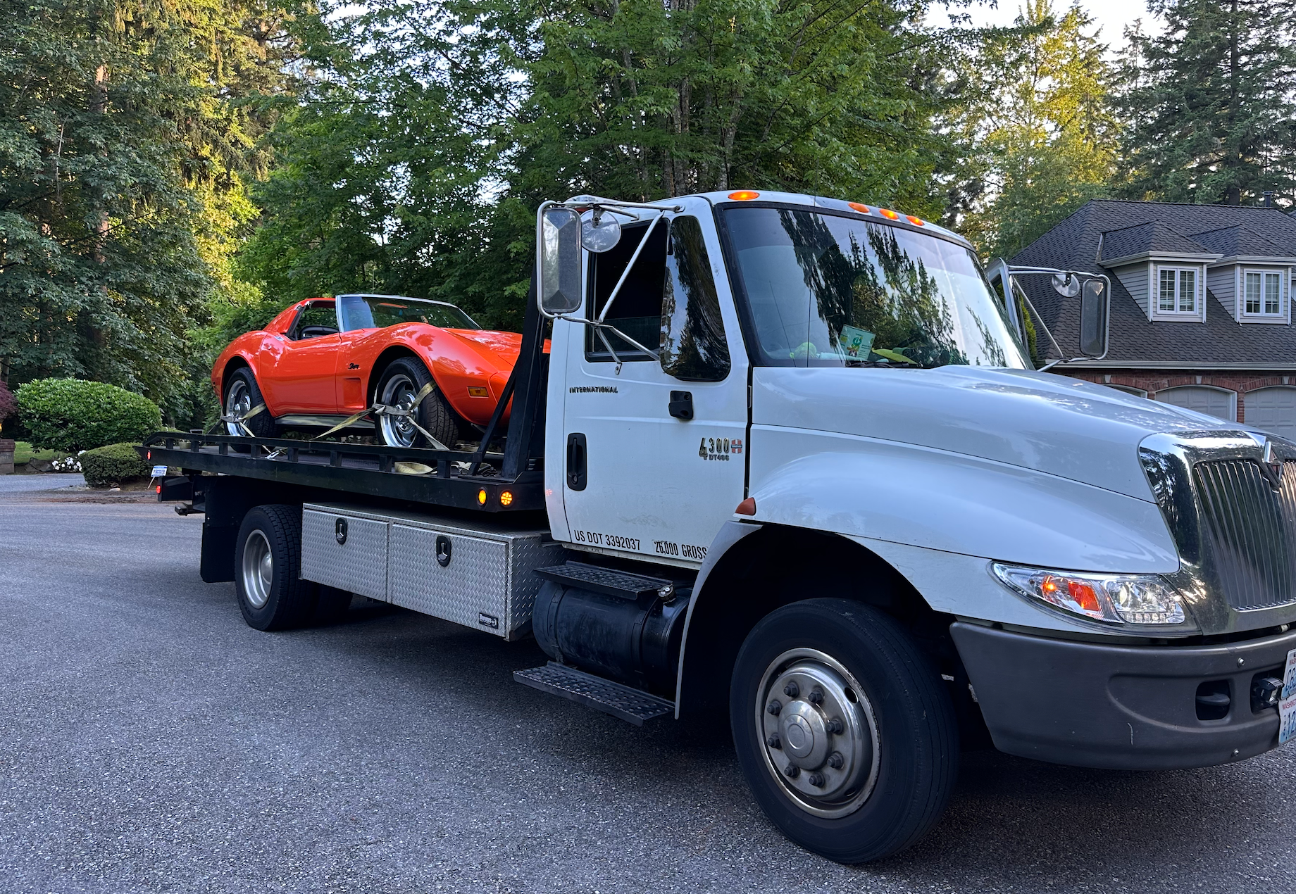 A tow truck is carrying a red sports car on the back of it.