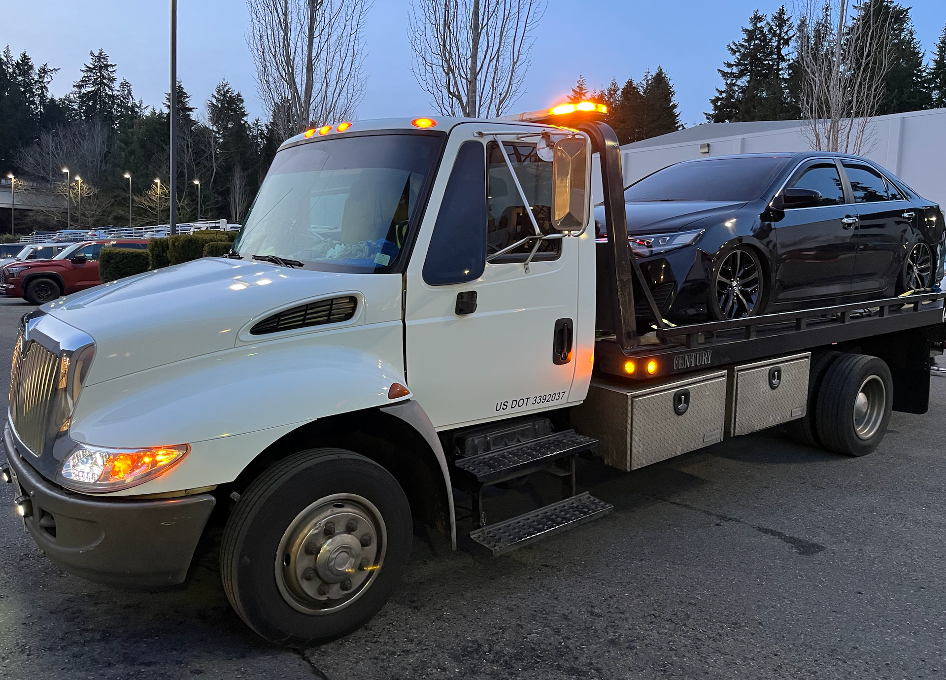 A tow truck with a car on the back is parked in a parking lot.