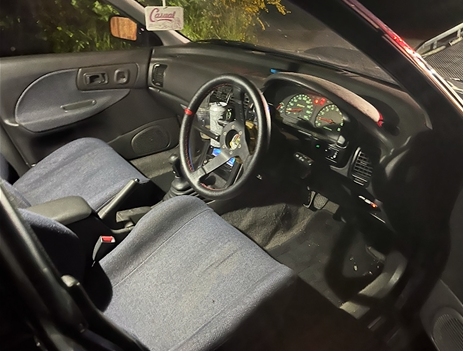Car interior with gray seats, black dashboard, and a custom steering wheel at night