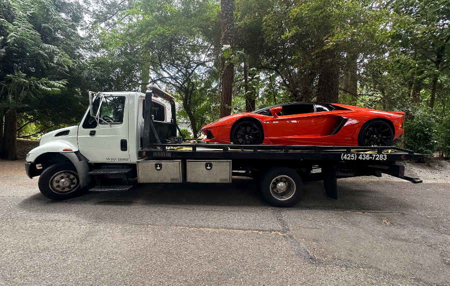 Orange sports car on a flatbed tow truck parked on a tree-lined street