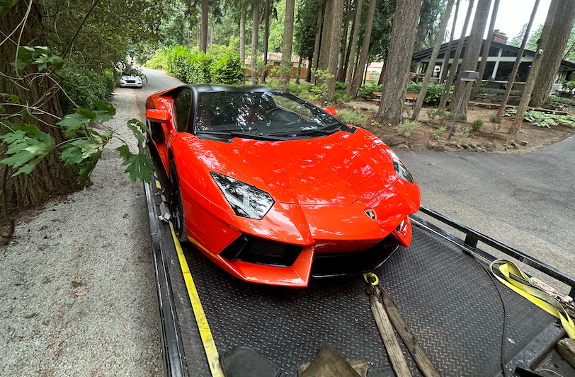Red sports car on a trailer on a wooded roadside track