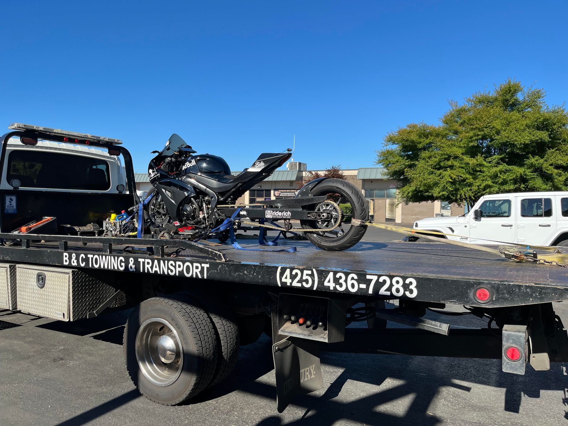 Tow truck hauling a crashed motorcycle on a flatbed in a sunny parking lot