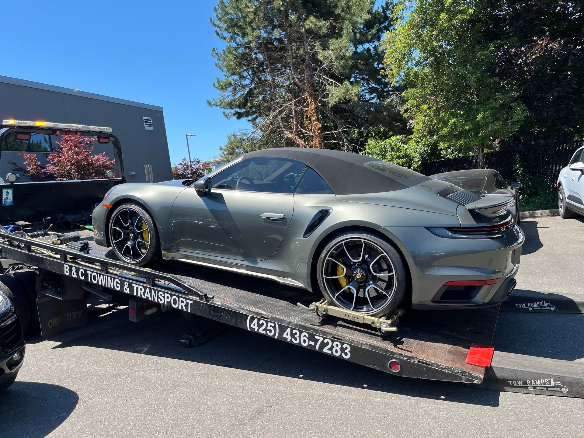 Gray sports car on a tow truck trailer, parked outdoors under a blue sky.