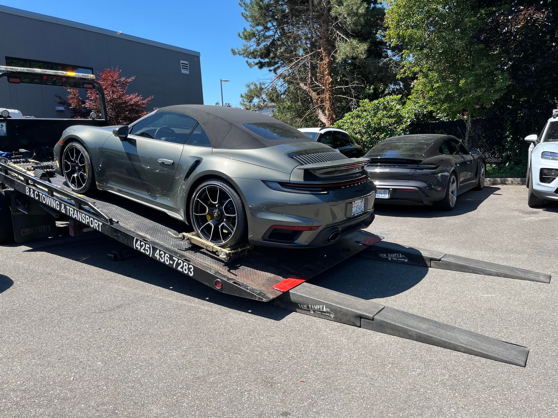 Gray sports car on a flatbed trailer in a parking lot, with another car behind it.