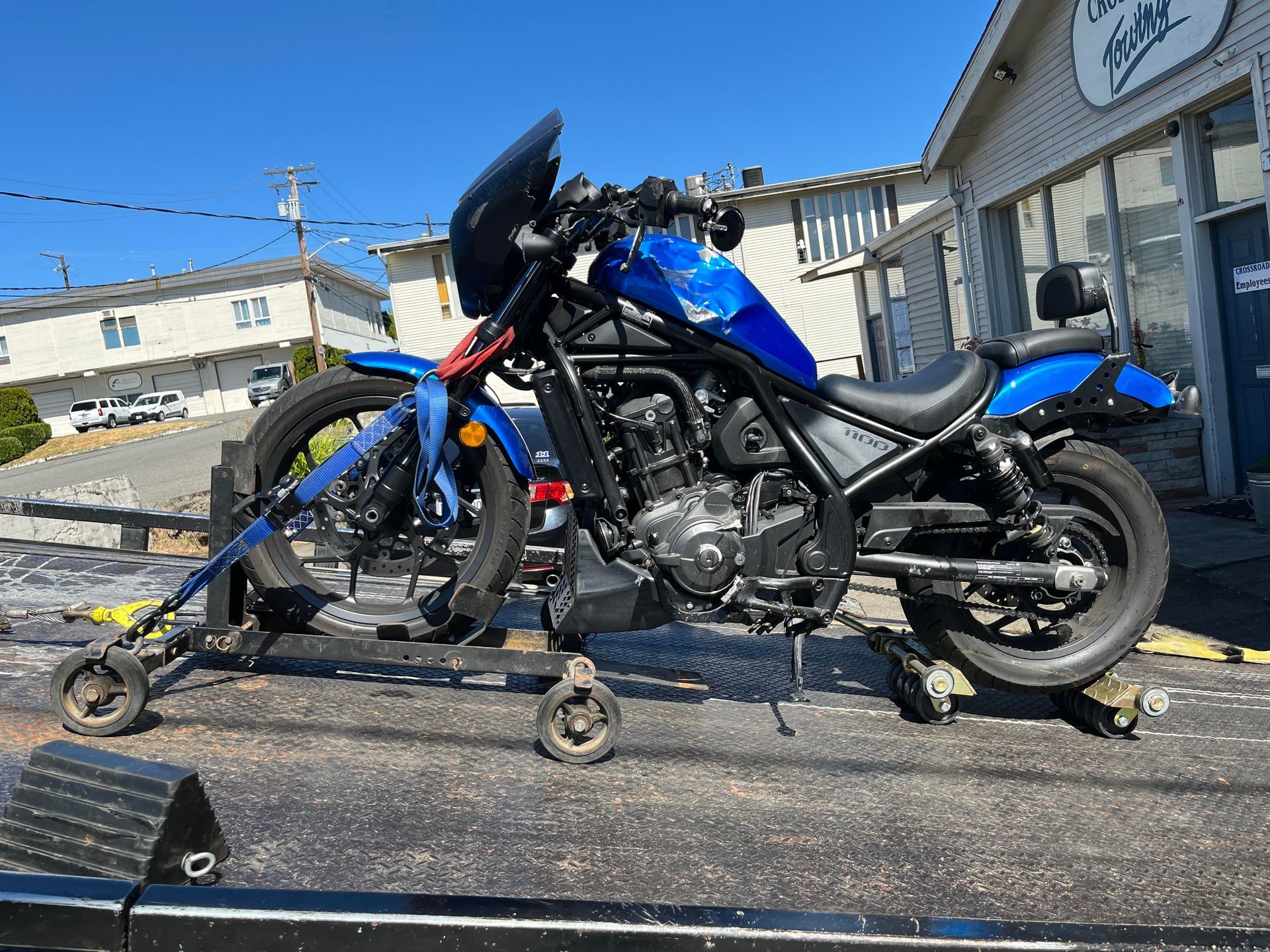 Blue motorcycle with support stands on a trailer outside a building in bright sunlight