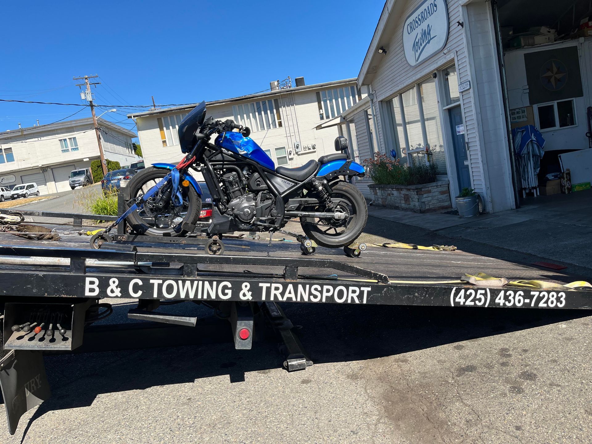 Blue motorcycle on a B&C Towing & Transport flatbed truck outside a building
